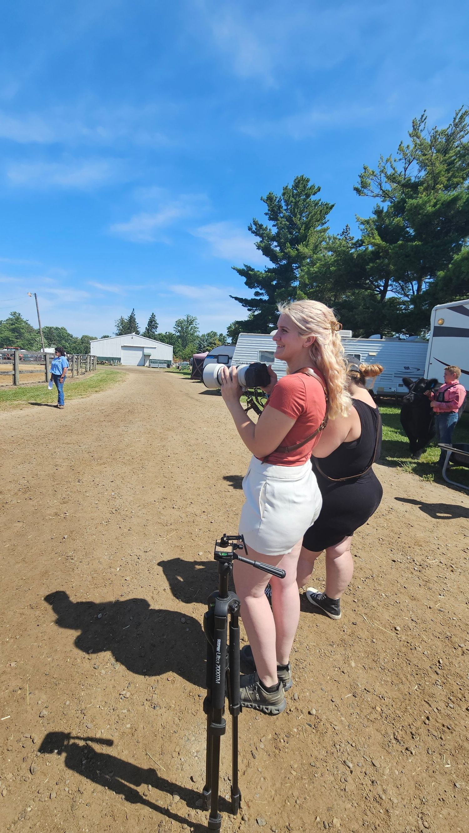 Photographers with cameras on tripods capturing shots on a dirt path on a sunny summer day with RVs in background.