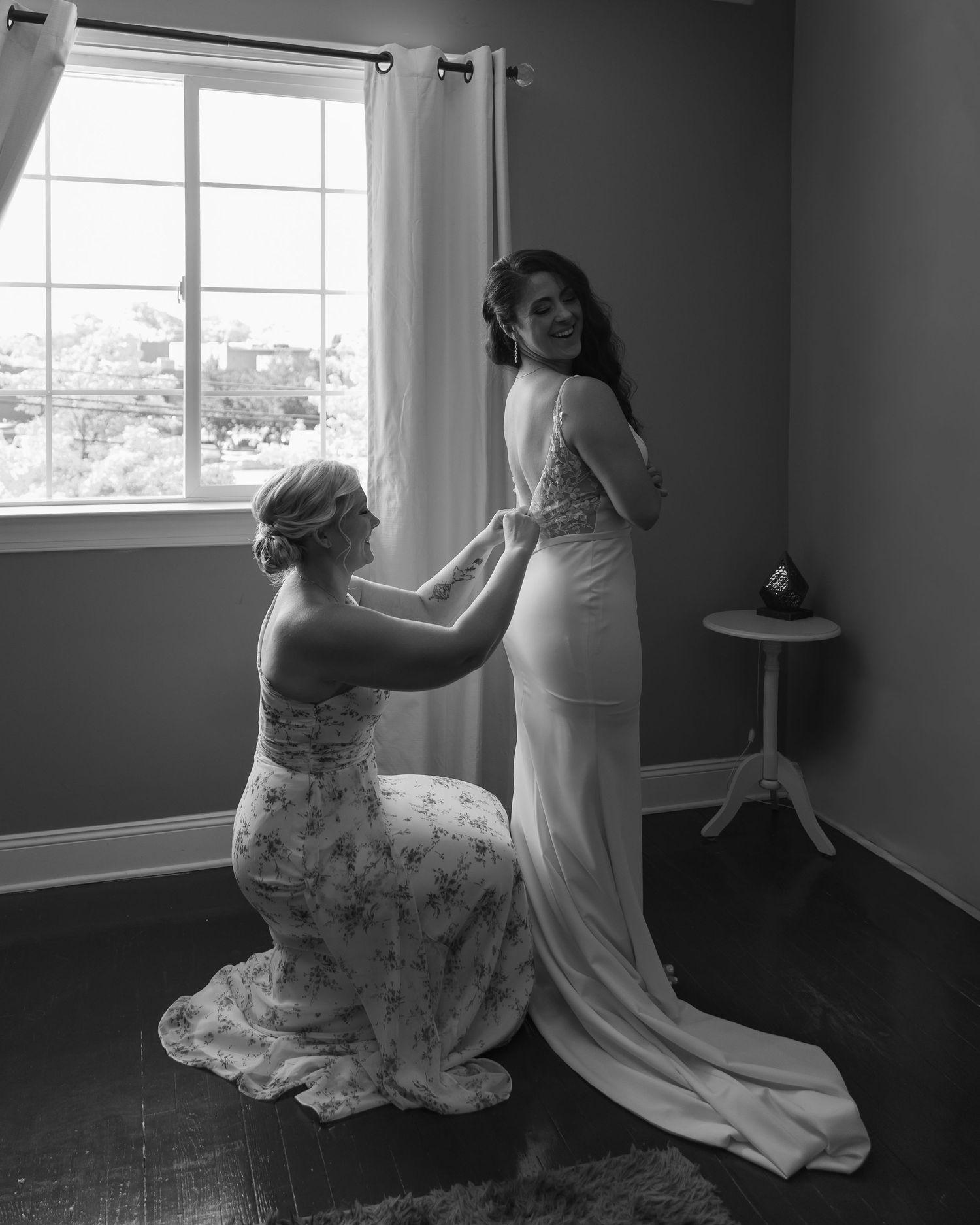 A black and white sequence of four photos showing someone dancing in a dress by a window.