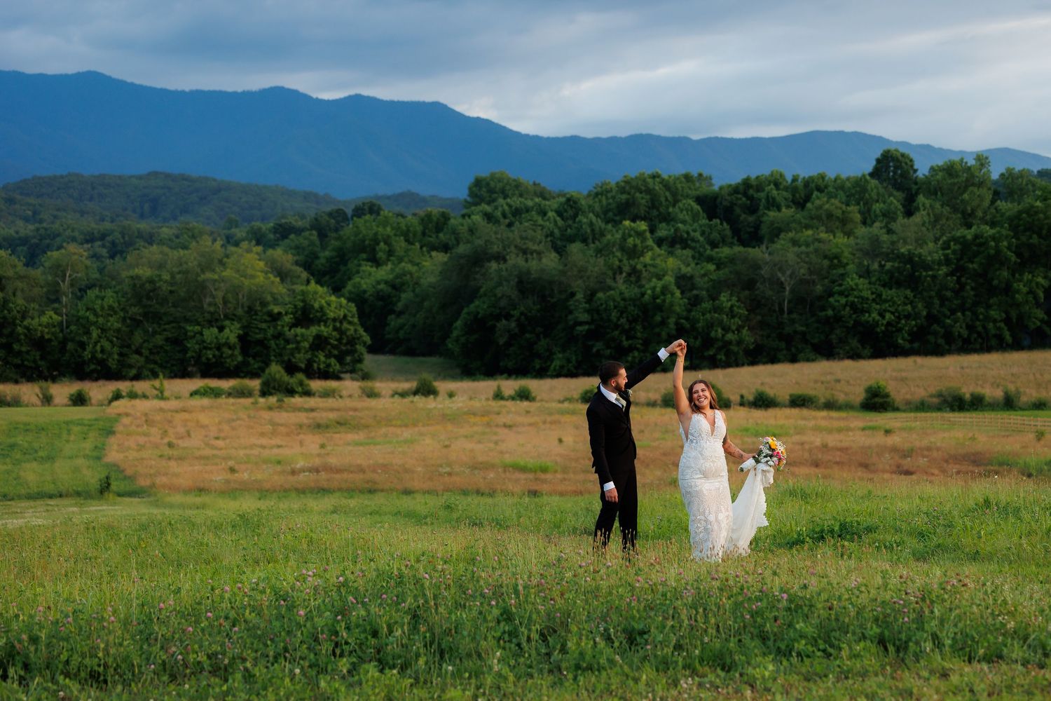 Bride and groom celebrate in a lush green meadow with stunning Blue Ridge Mountain views on their wedding day.