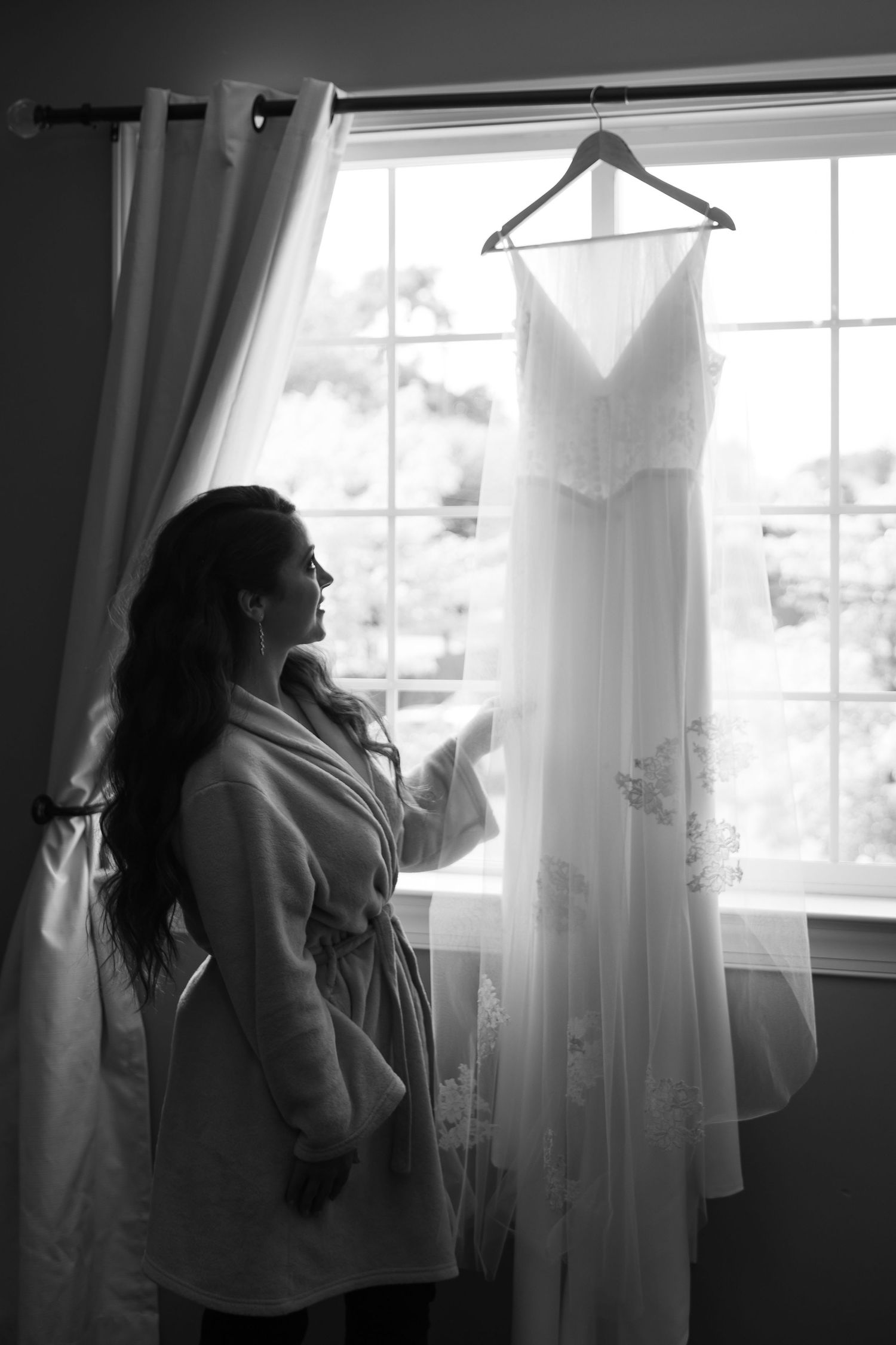 A black and white photo series showing a person standing by a window with flowing curtains in different poses.