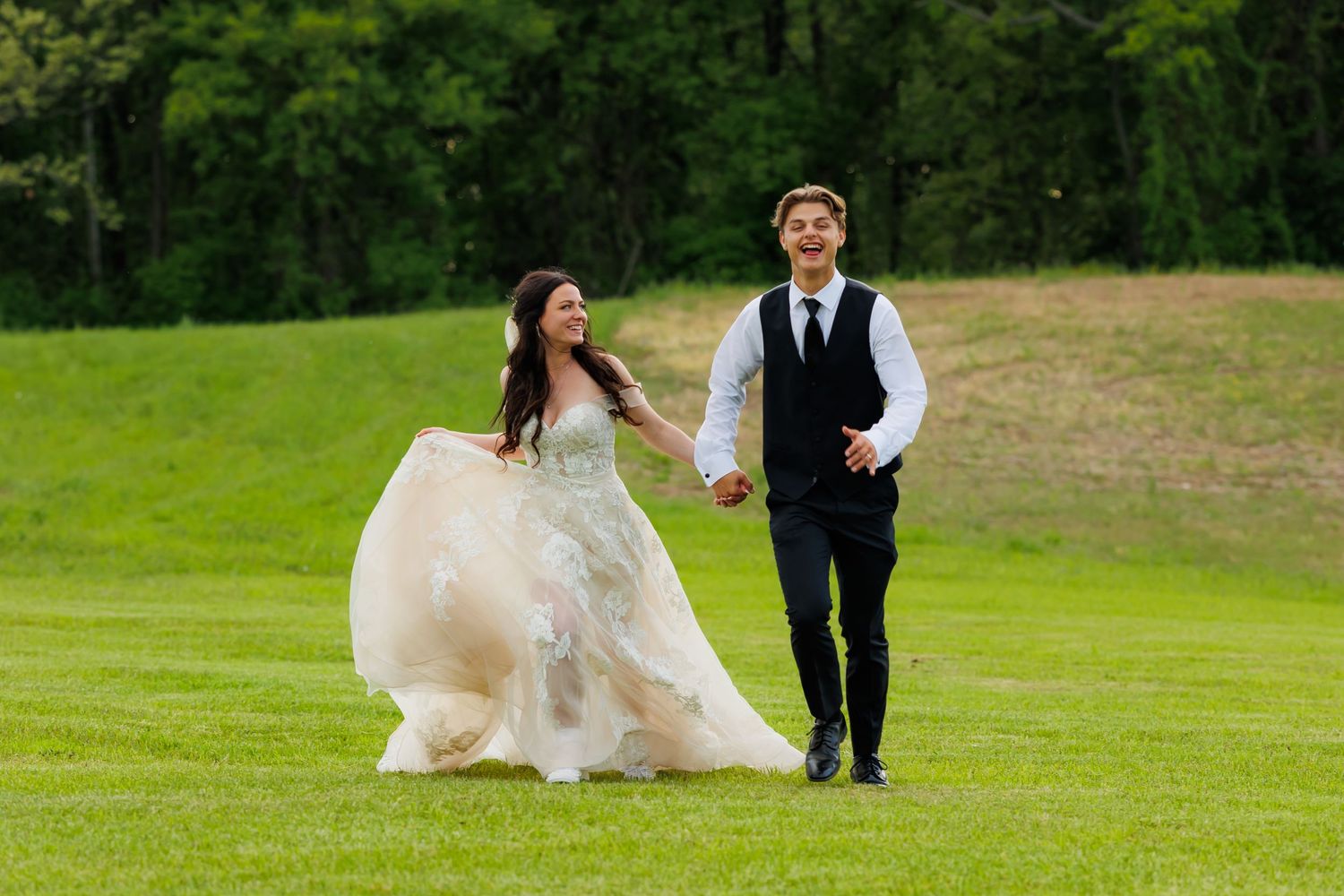A couple runs together on a lush green lawn, with the bride's white dress flowing elegantly in the breeze.