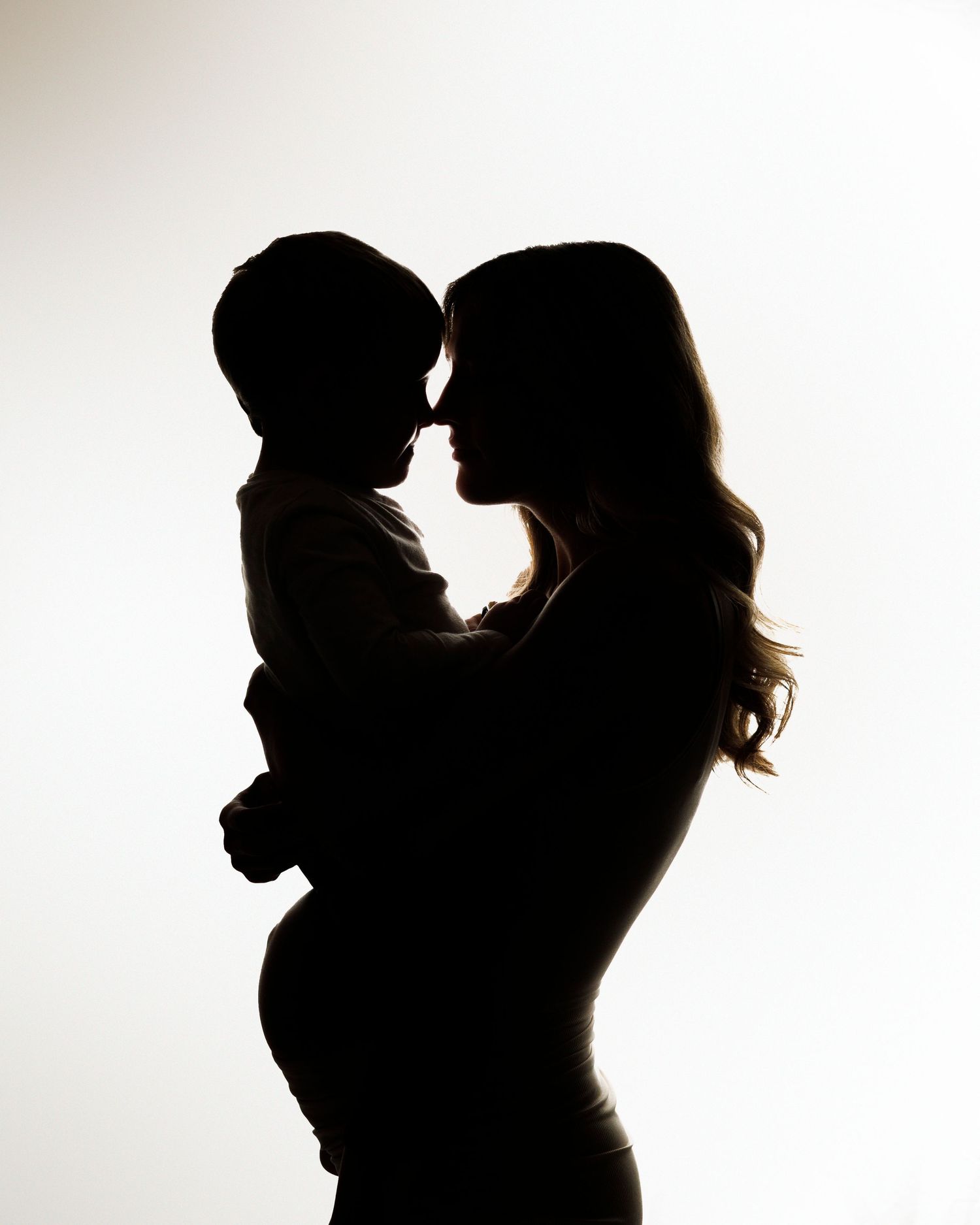 Silhouette portrait of mother and child touching noses against white background.