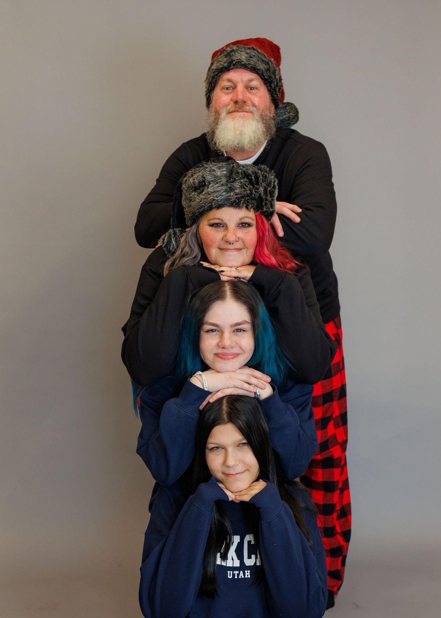 Creative portrait of four people stacked vertically wearing winter clothing against grey background.