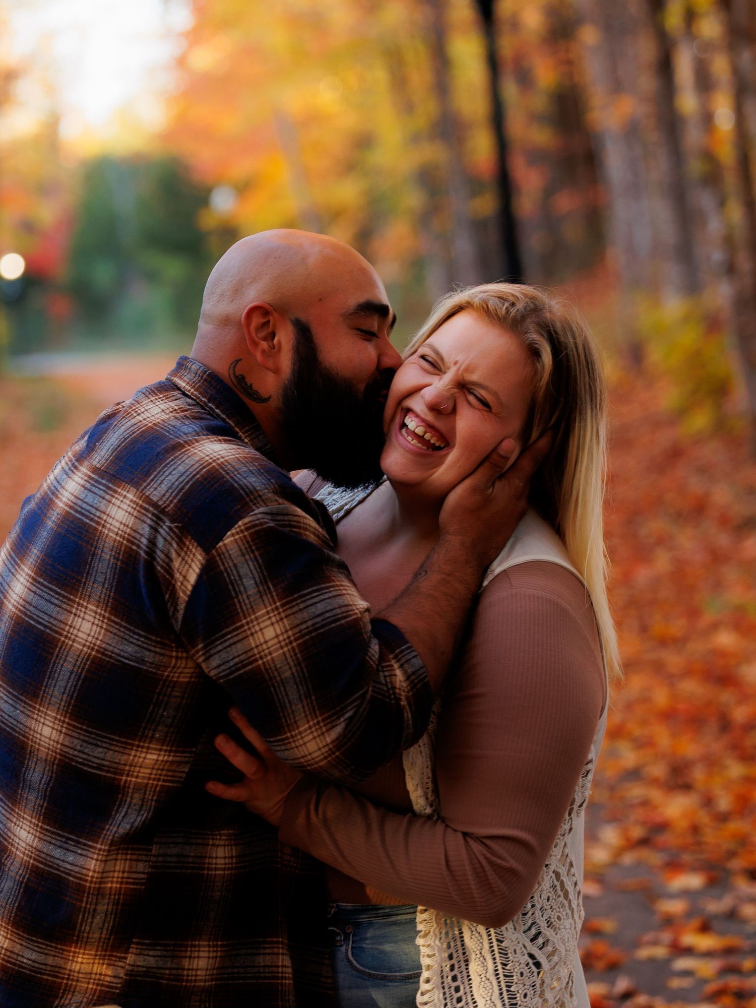 A couple shares romantic moments in a fall setting with colorful autumn leaves on the ground.
