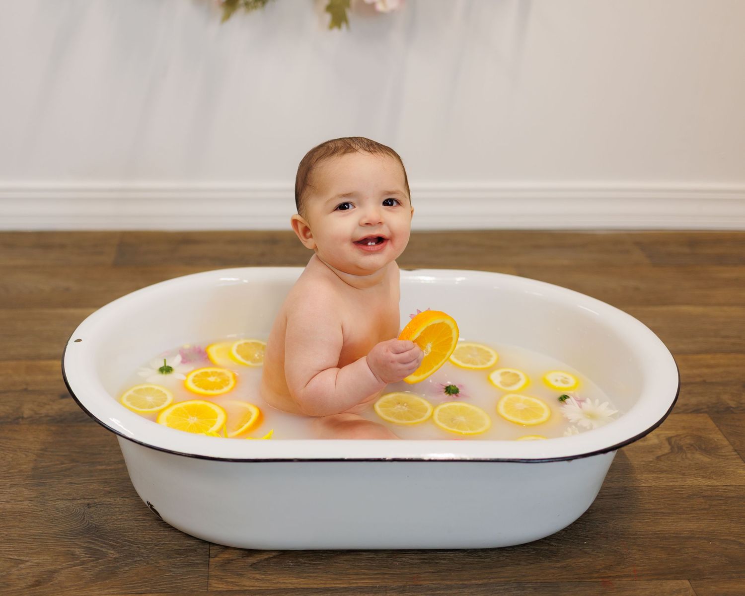 Smiling baby sitting in a white enamel tub filled with lemon slices and water for a milestone photo session.