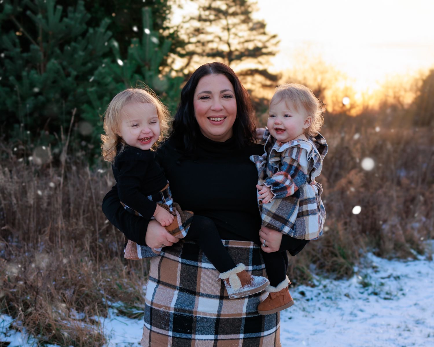 Winter family portrait with plaid skirt against snowy landscape at sunset.
