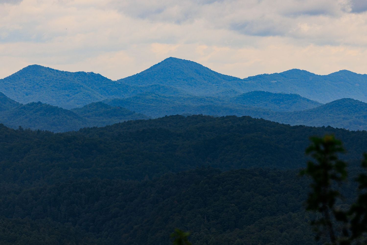 Rolling blue mountains fade into the distance under a cloudy sky in a scenic landscape view.