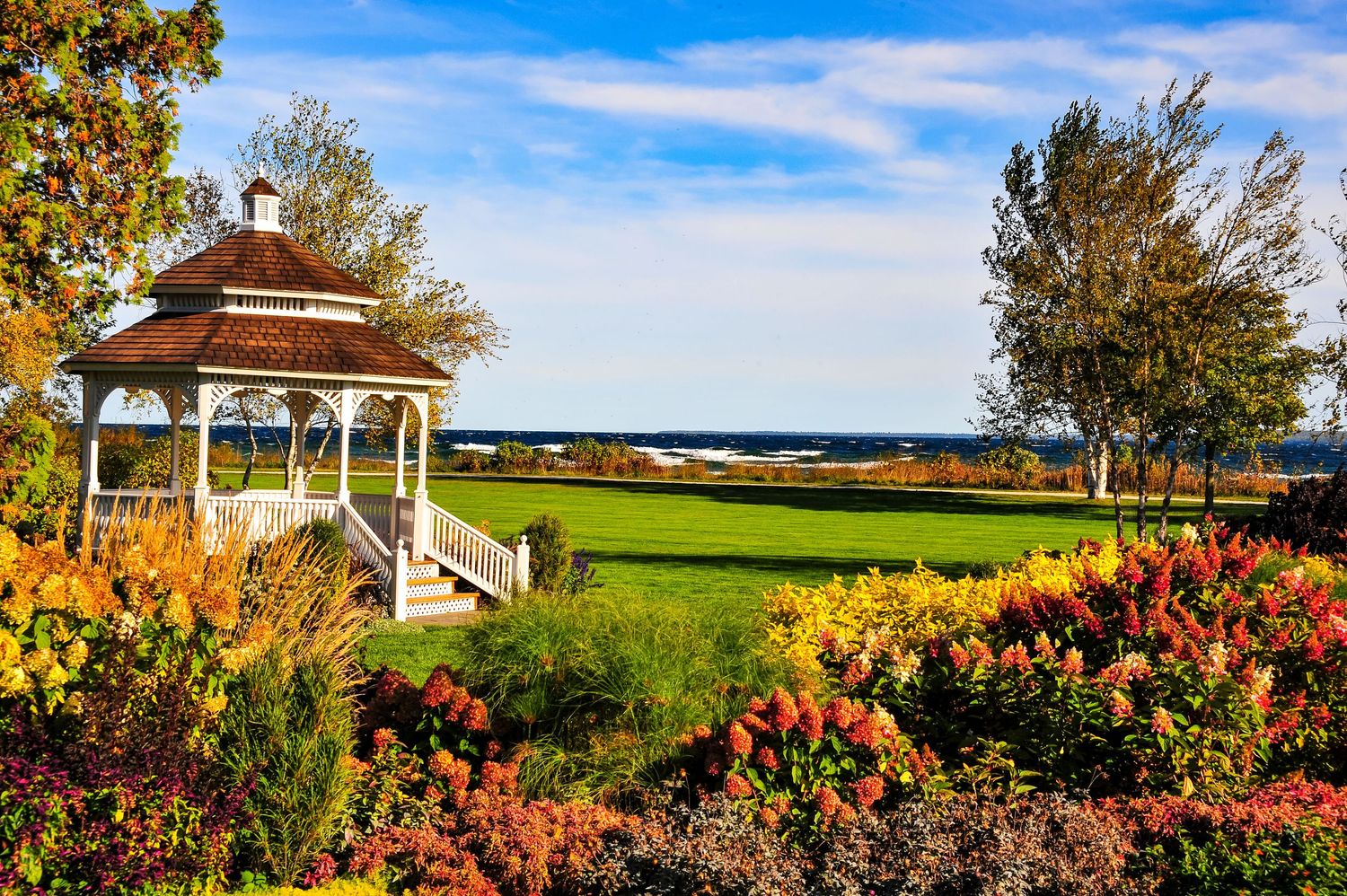 A panoramic coastal landscape featuring vibrant fall foliage, a white gazebo, and rolling green hills overlooking the ocean.