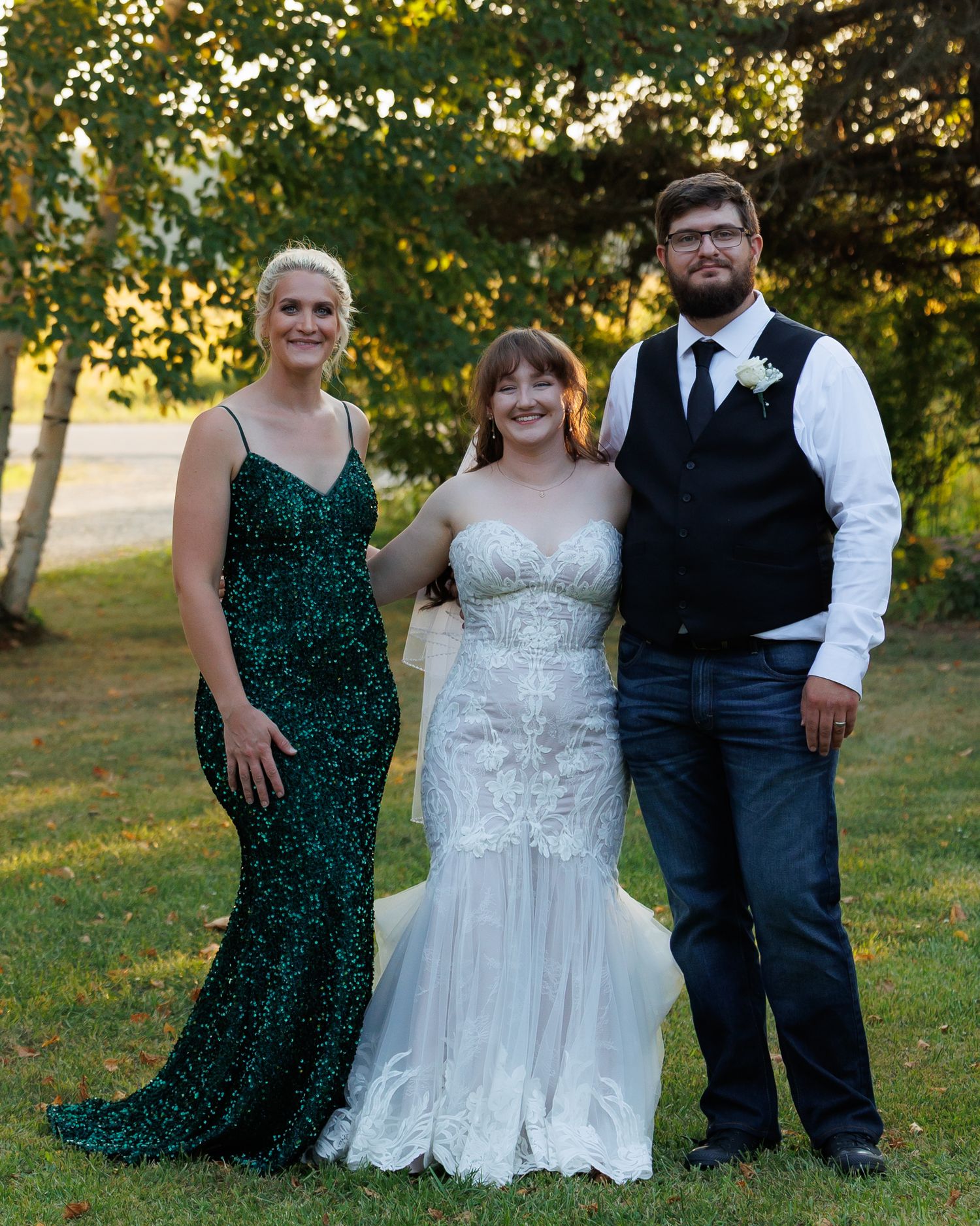 Wedding party stands together outdoors in green dresses and formal attire during golden hour.