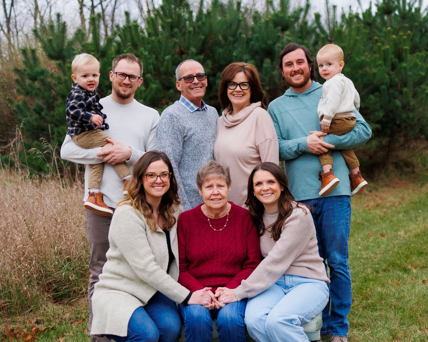 Extended family portrait taken outdoors with pine trees in the background.