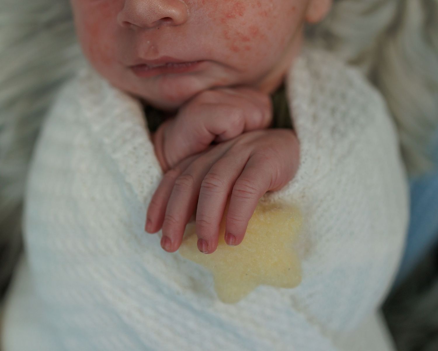 Small hand resting on white knit fabric with a yellow stain.