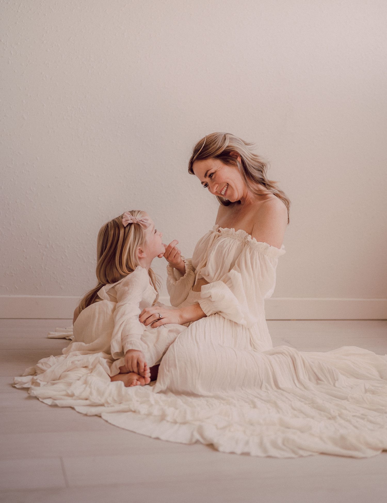 A series of artistic maternity photos showing a woman in a flowing white dress reclining gracefully against a neutral backdrop.
