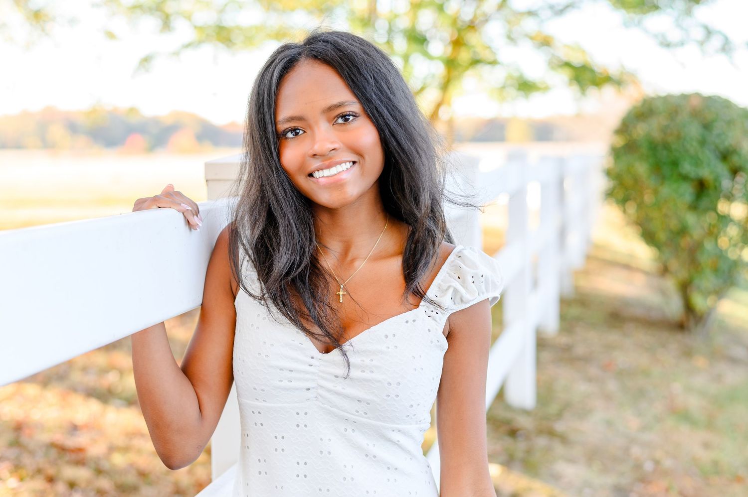 Graduate in white lace dress smiles brightly during outdoor photo session.