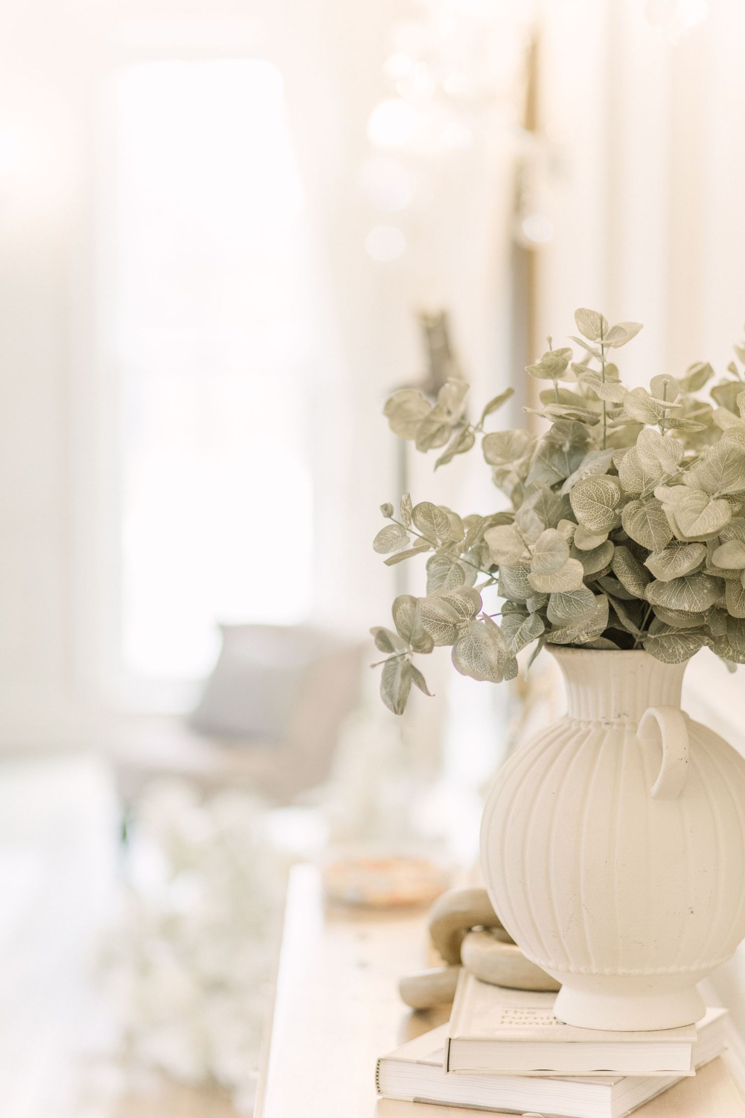 White ceramic vase filled with eucalyptus branches on a light surface in a bright, airy setting.