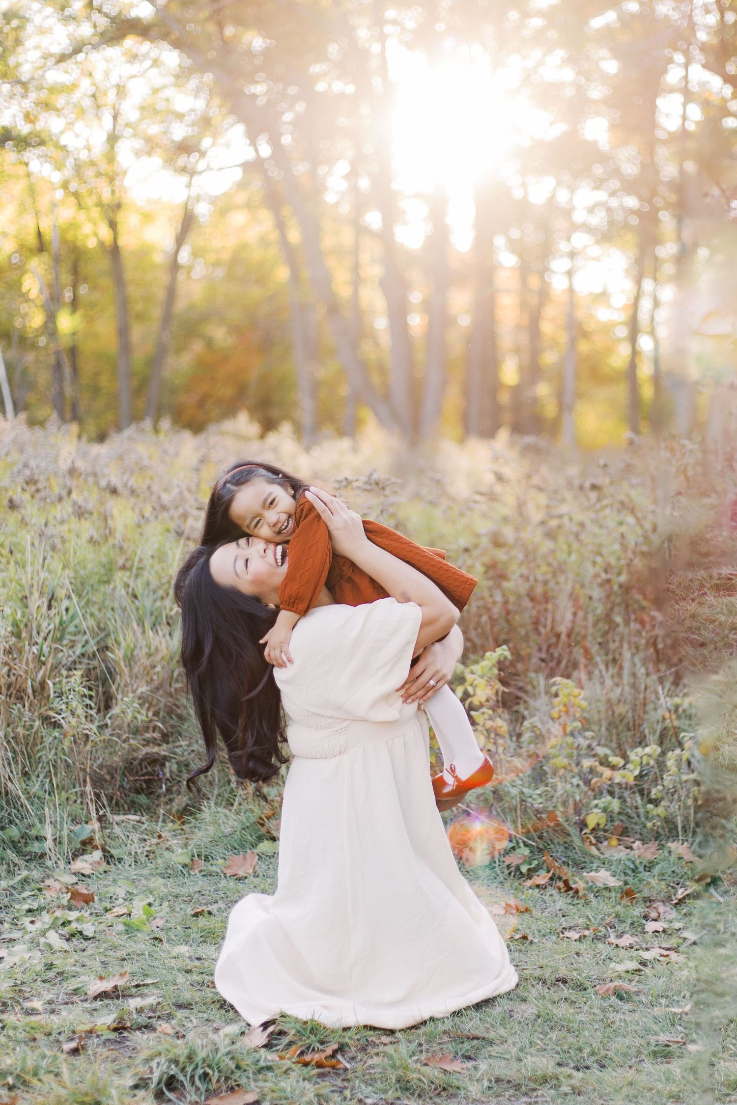 Woman in flowing white dress twirls joyfully in autumn forest setting with golden sunlight filtering through trees.