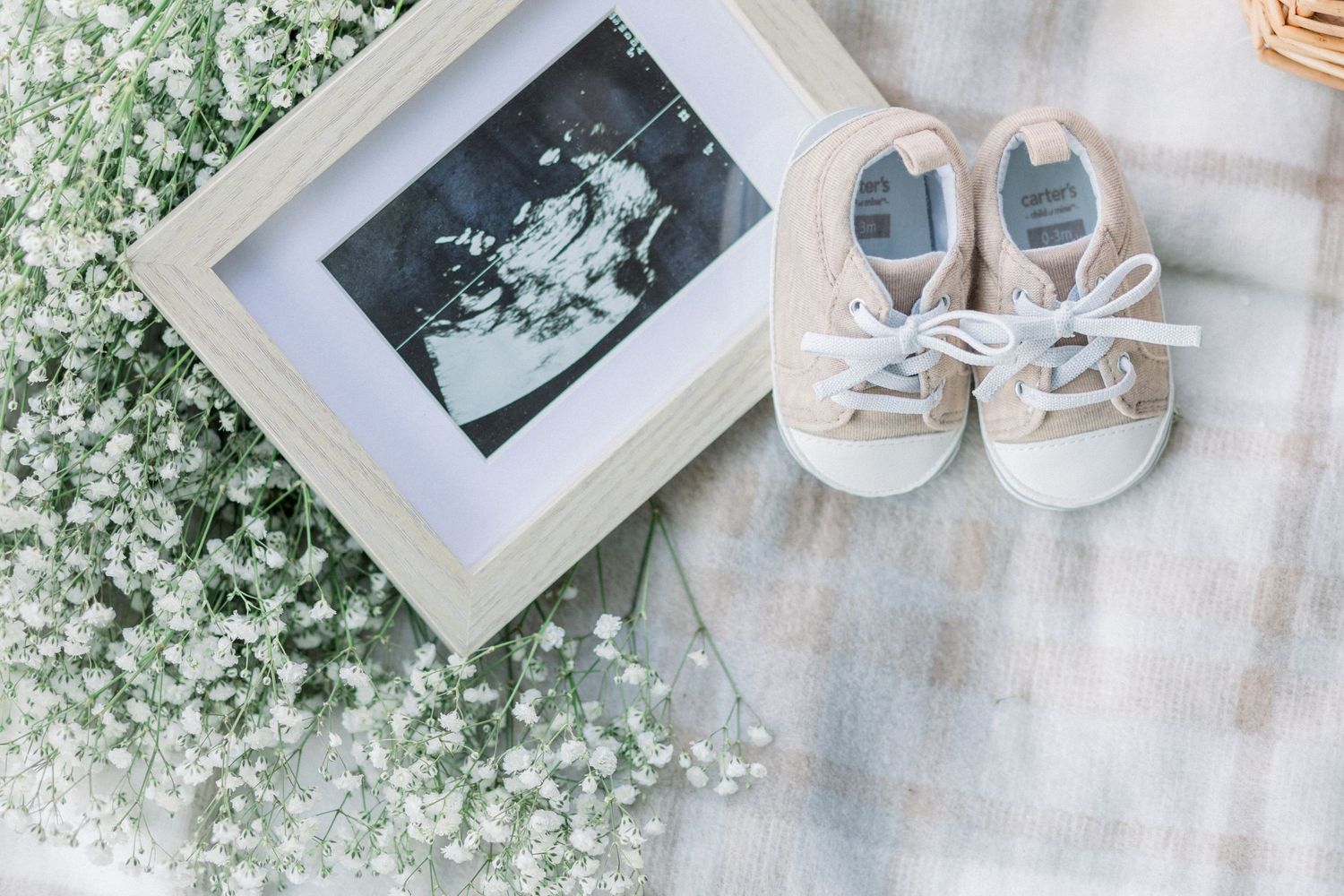 Delicate white baby's breath flowers surround a framed photo and tiny shoes on a light gray surface.