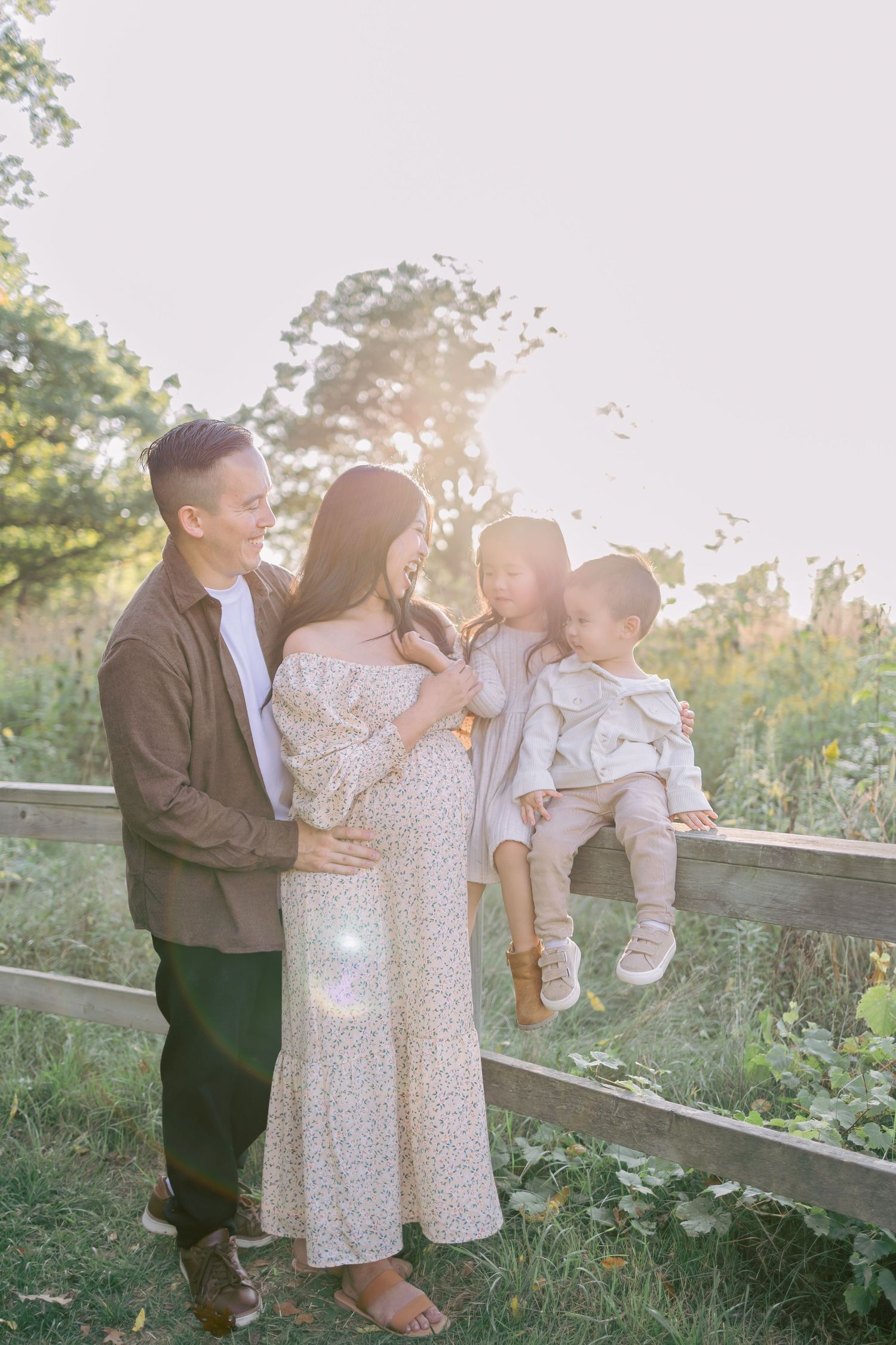 Family enjoying a tender moment together at sunset by a wooden fence in a field with golden sunlight.