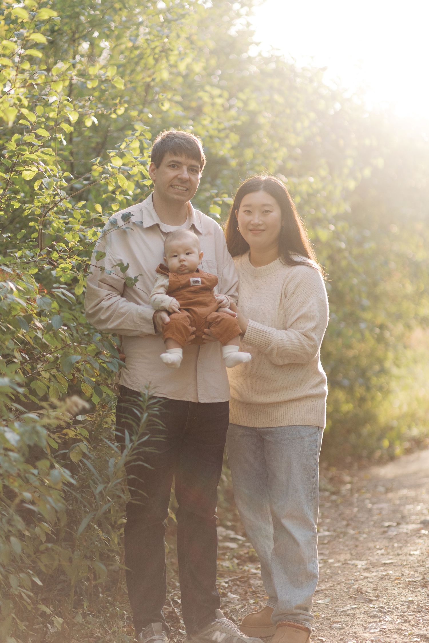 Family enjoying a sunny afternoon walk together on a nature trail surrounded by green foliage.