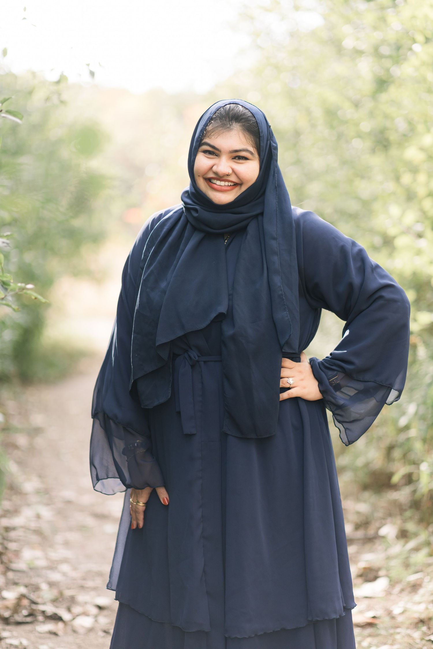 A series of fashion photos showing a person wearing a navy blue hijab and abaya in an outdoor setting with trees.