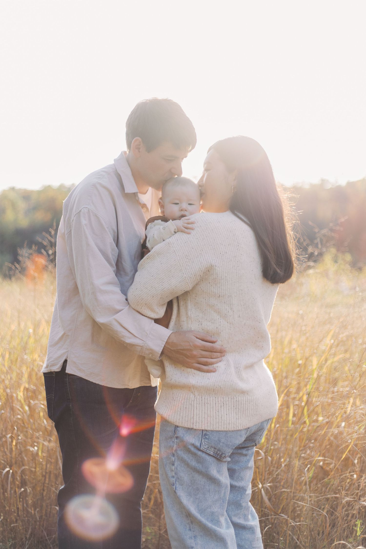 A couple shares intimate moments in a sunlit field of tall grass during golden hour.