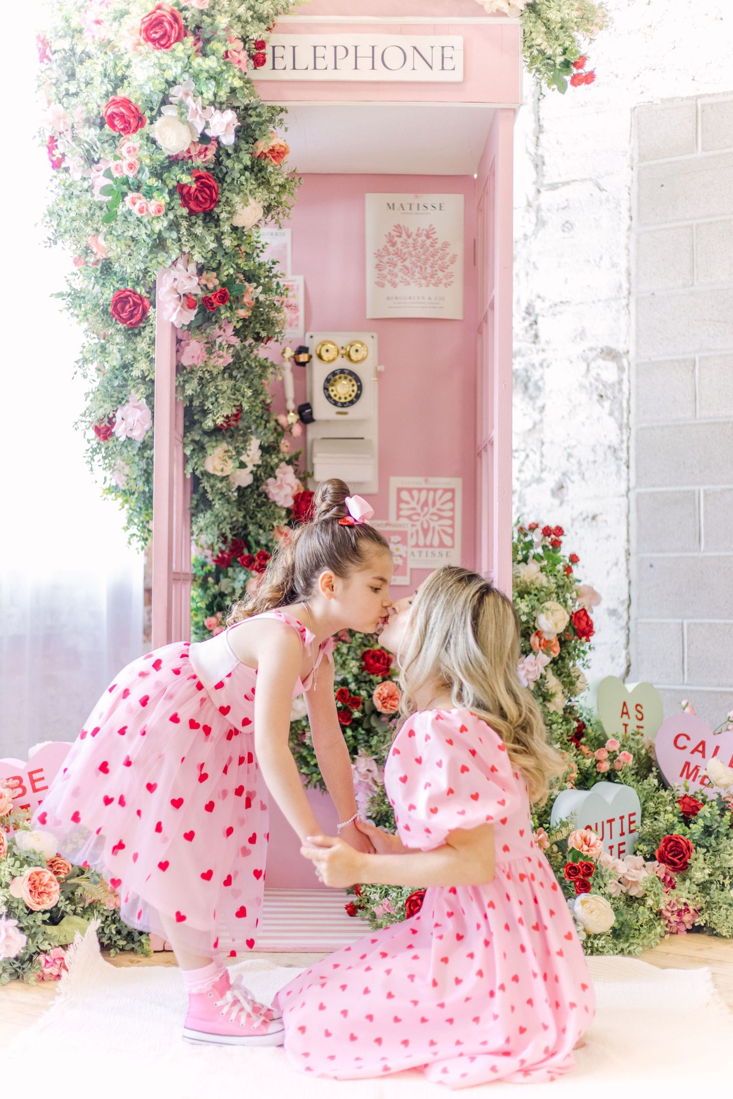 Pink and white polka dot dresses complement a romantic telephone booth setting adorned with climbing roses and floral decor.