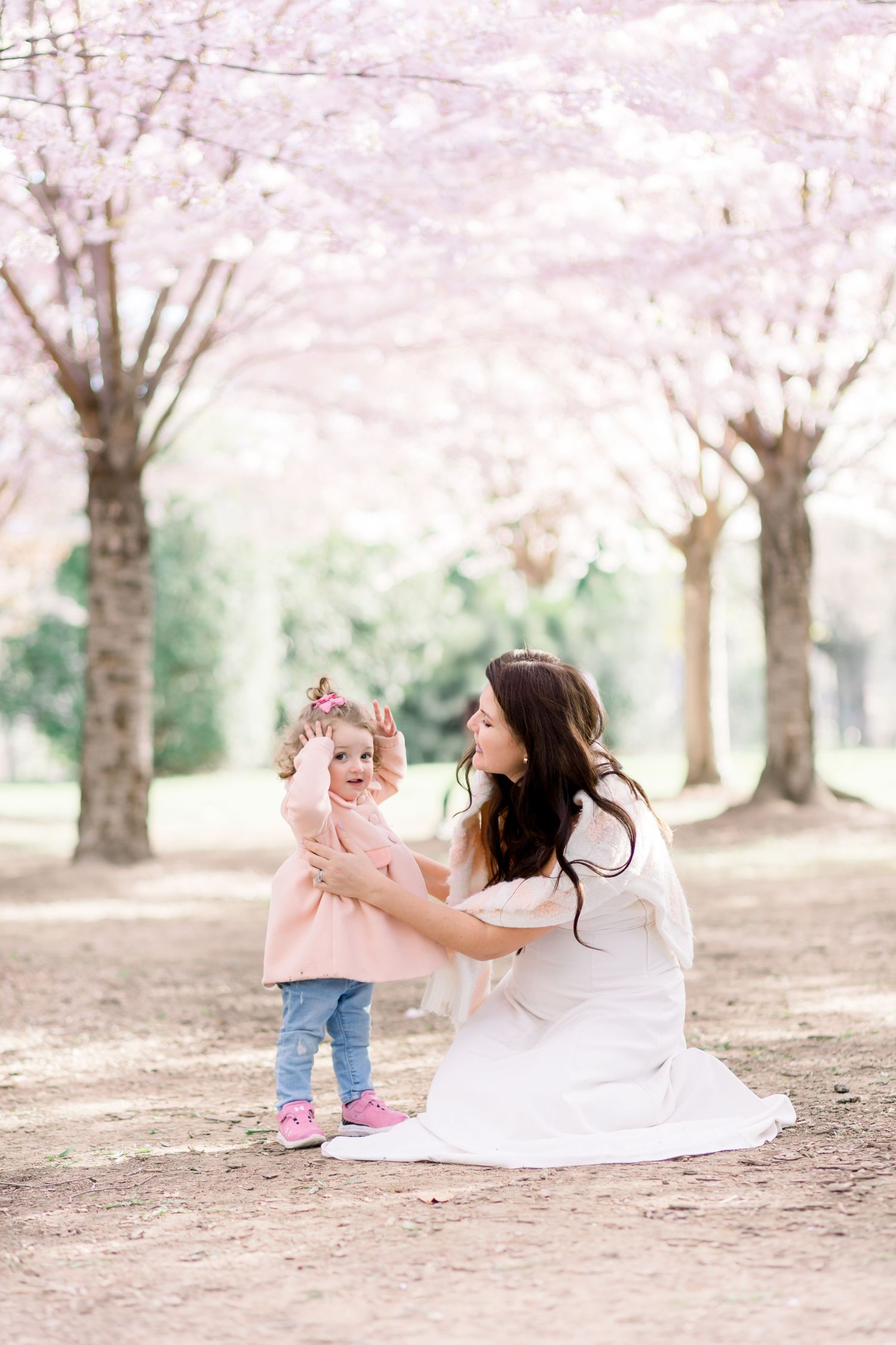 A parent and toddler share a joyful moment together while sitting under blooming cherry blossom trees in a park.