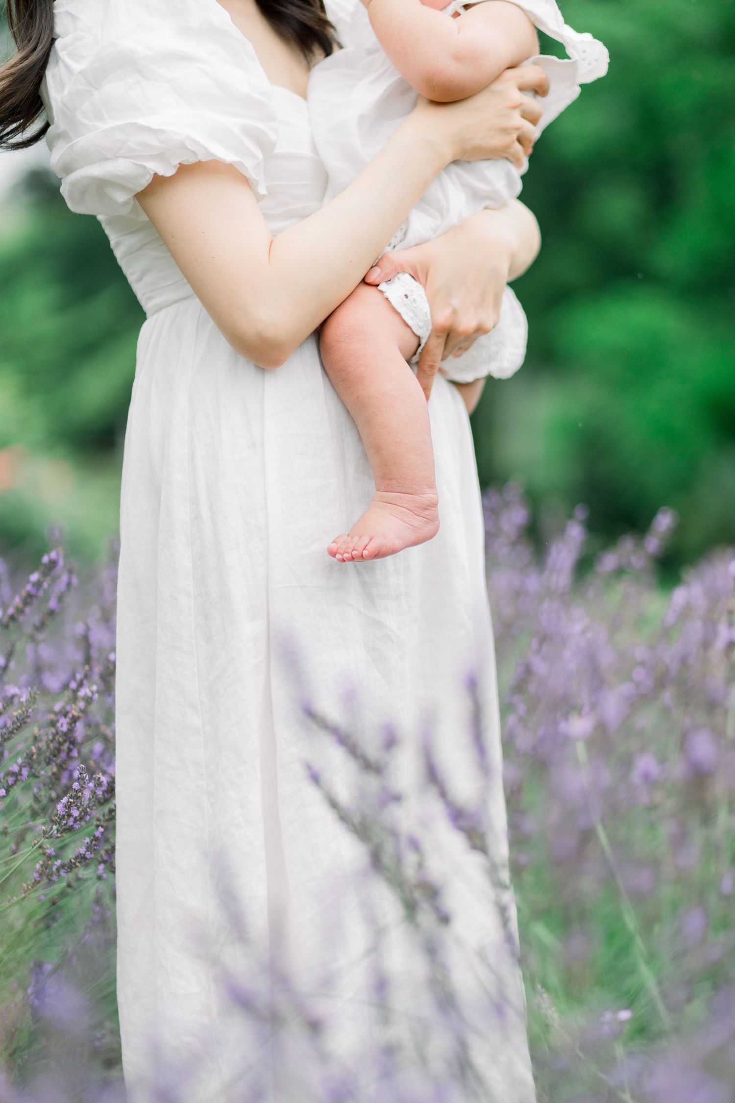 A figure in a flowing white dress stands among blooming purple lavender flowers in a garden setting.