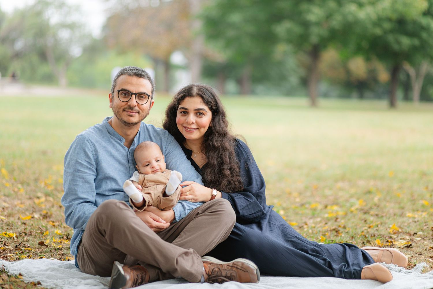 Family sitting together on blanket in park during fall season.