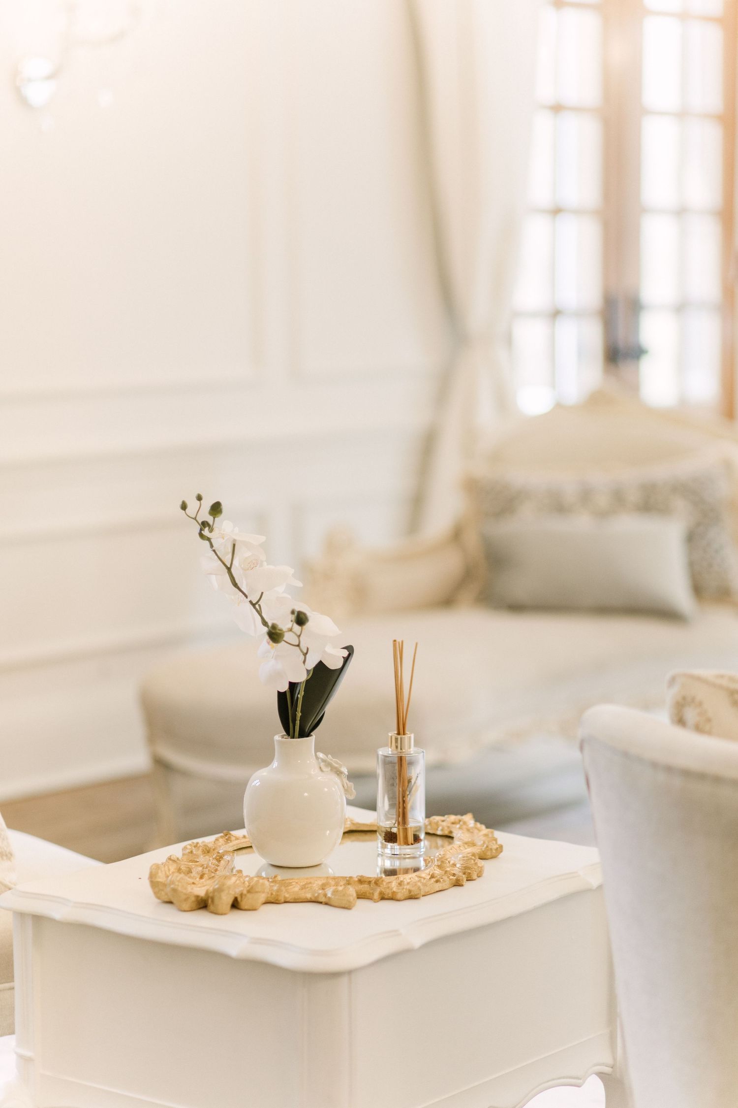 Elegant white living room with orchid in vase and diffuser on decorative tray, styled in minimalist coastal decor.