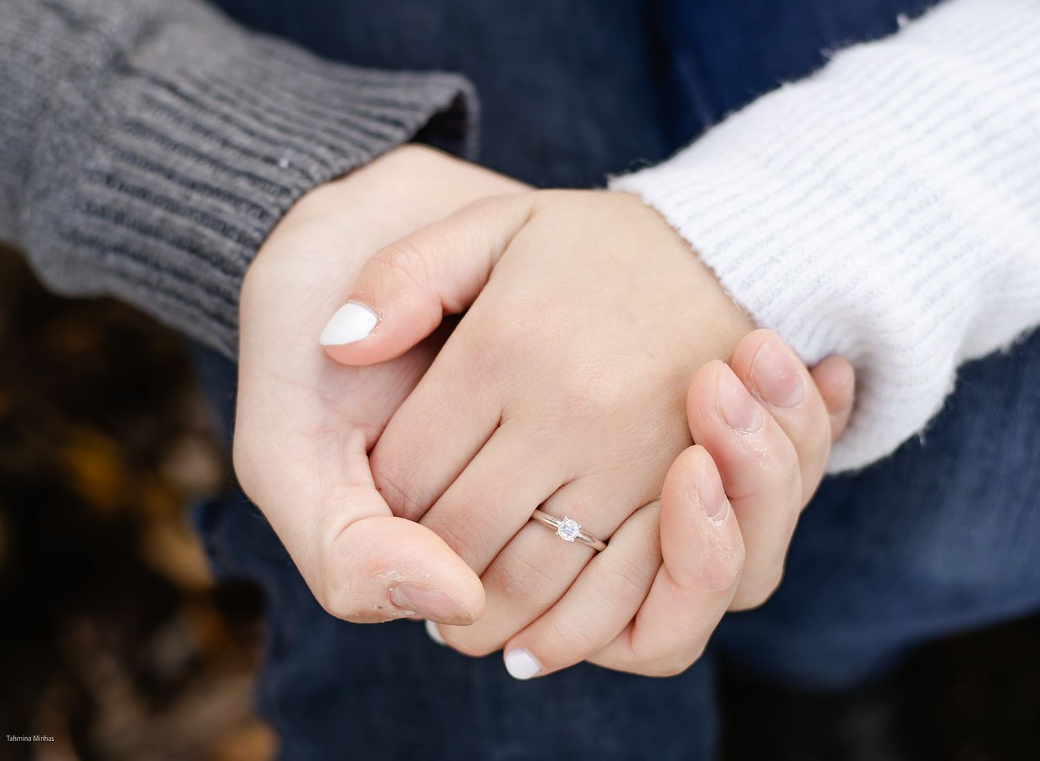 Close-up shot of hands wearing engagement ring with white sweater sleeve in the background.