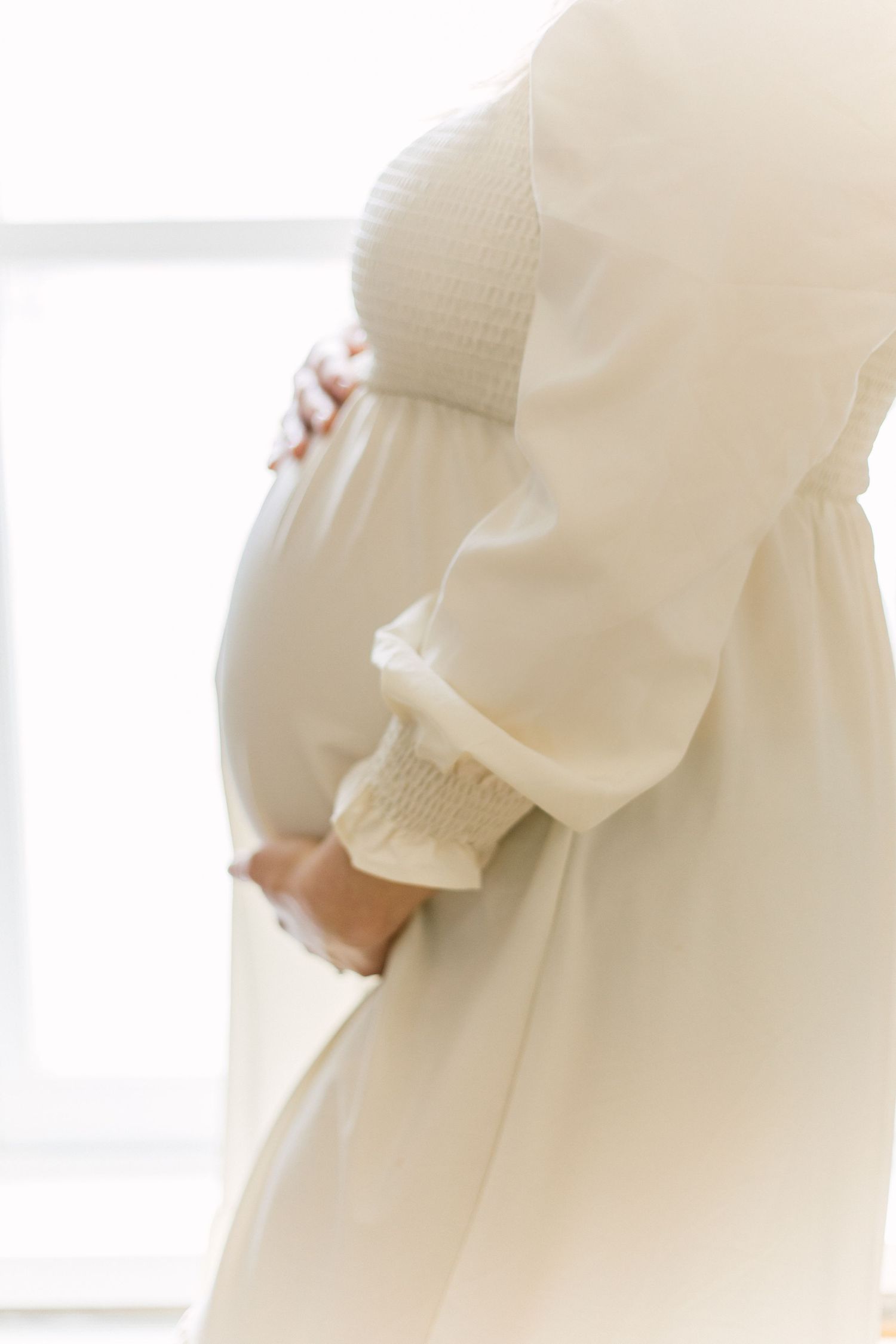 Close-up details of a flowing white maternity gown against a bright background.
