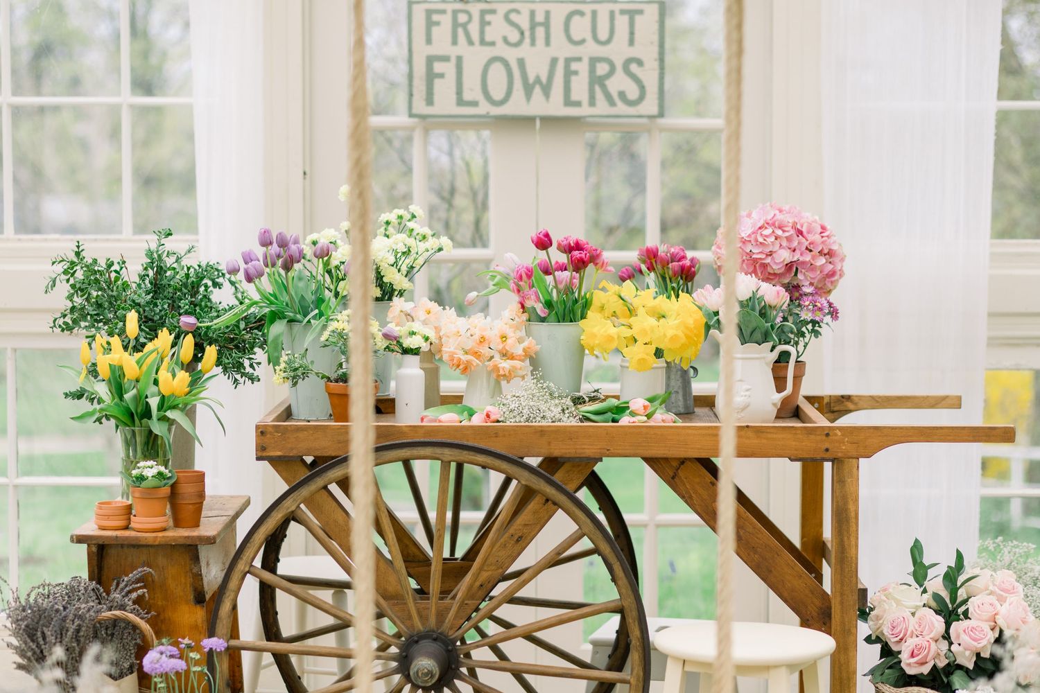 A bright flower shop interior with wooden display cases, fresh cut flowers, and large windows letting in natural light.