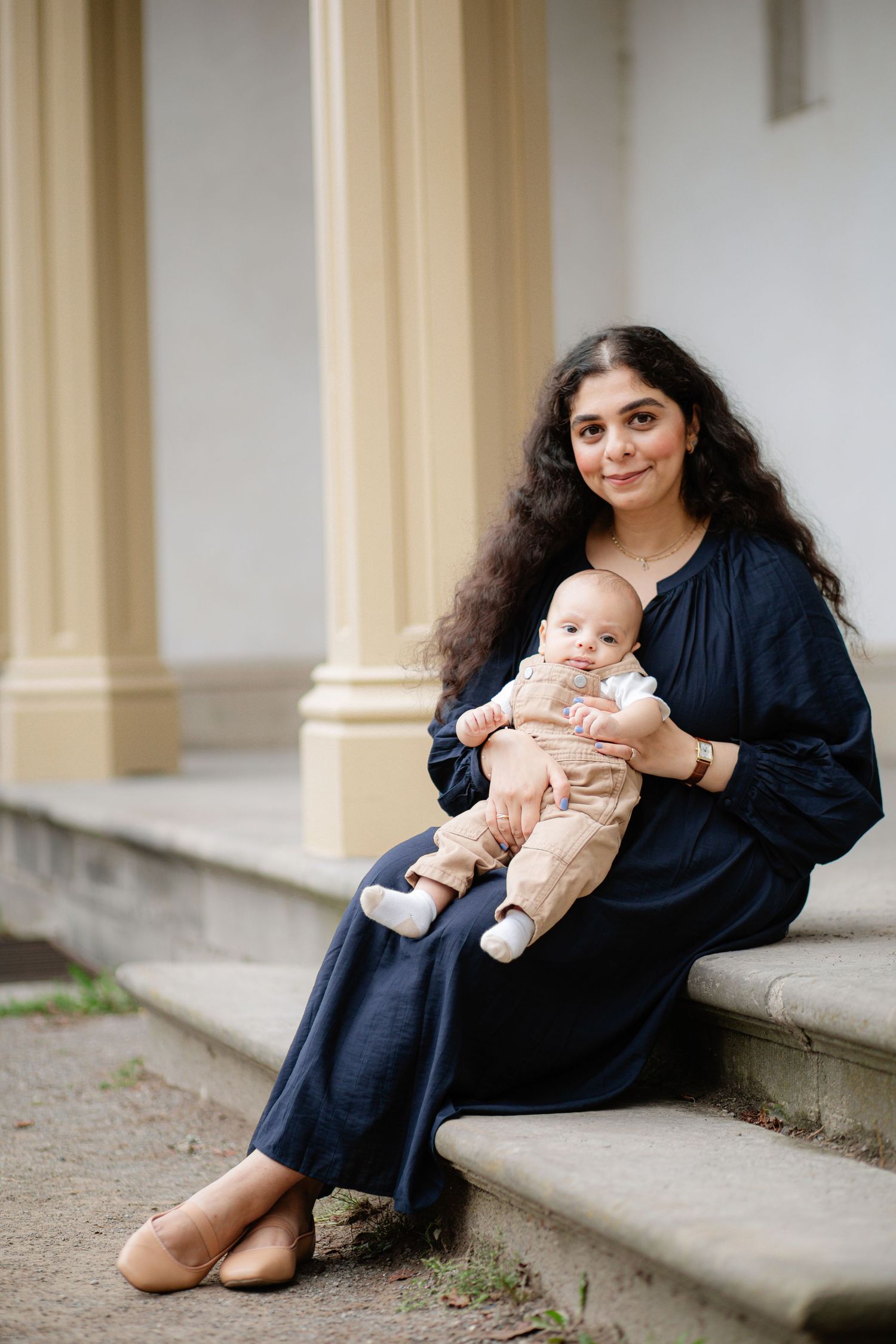 A person in a navy dress sits on stone steps holding a baby wearing light-colored clothes.