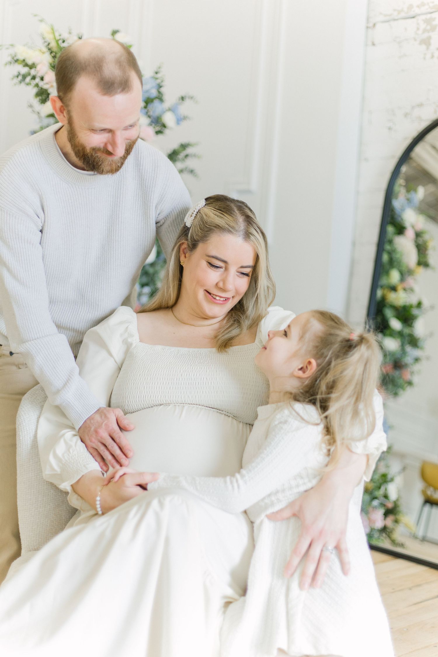 A sweet family moment as parents and child share tender moments together in a light, airy room with floral decor.