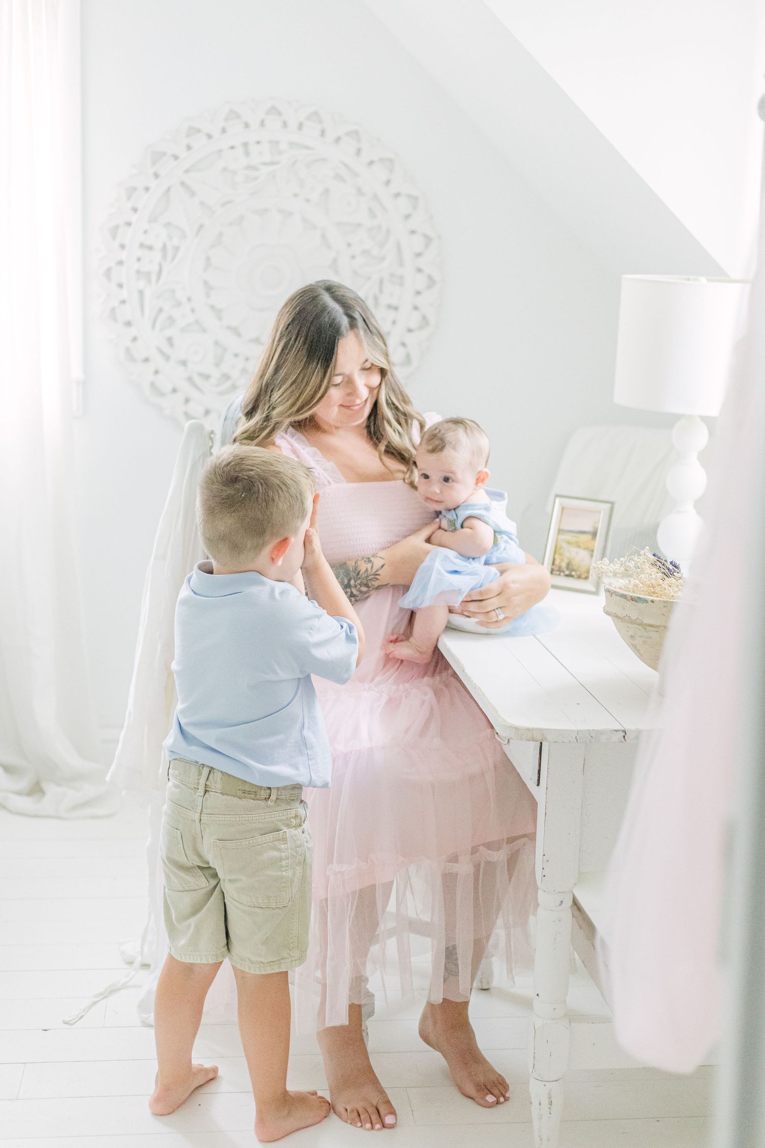 A toddler in khaki shorts dances with someone wearing a pink dress in an elegant white room with decorative details.