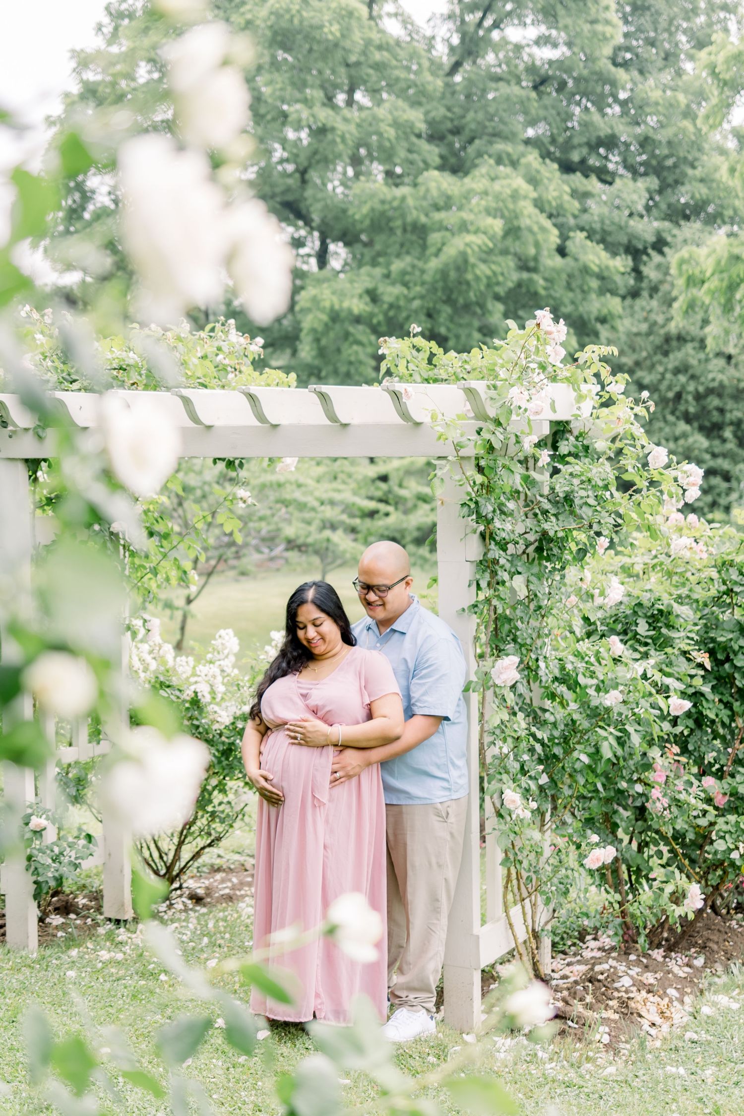 A couple shares an intimate moment together in a lush garden setting with white flowers and greenery.