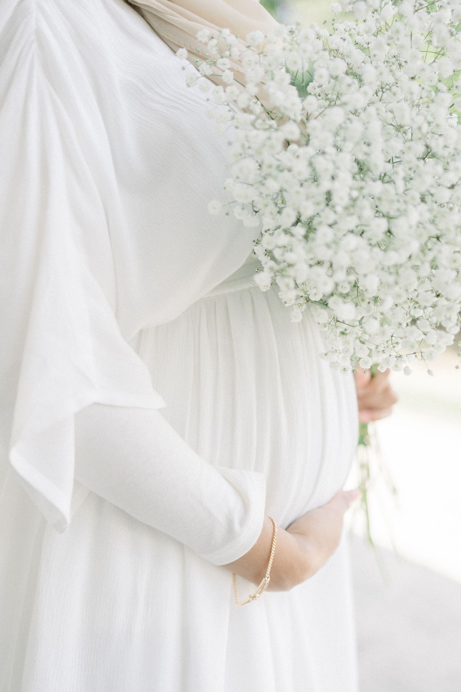 Woman in flowing white dress stands among delicate white floral blossoms in an ethereal spring garden setting.