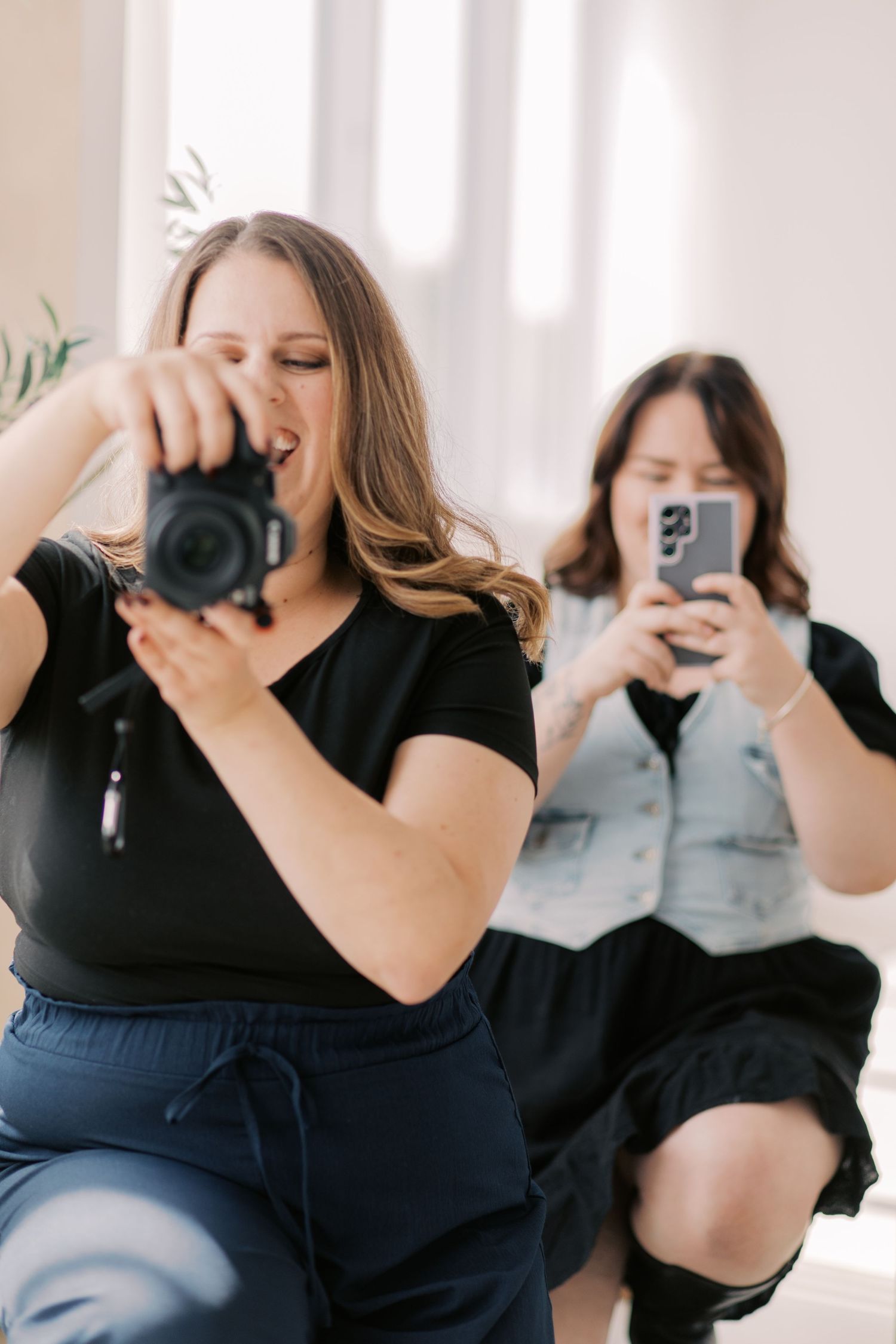 Two people in black outfits taking photos with cameras and phones in a bright indoor setting.