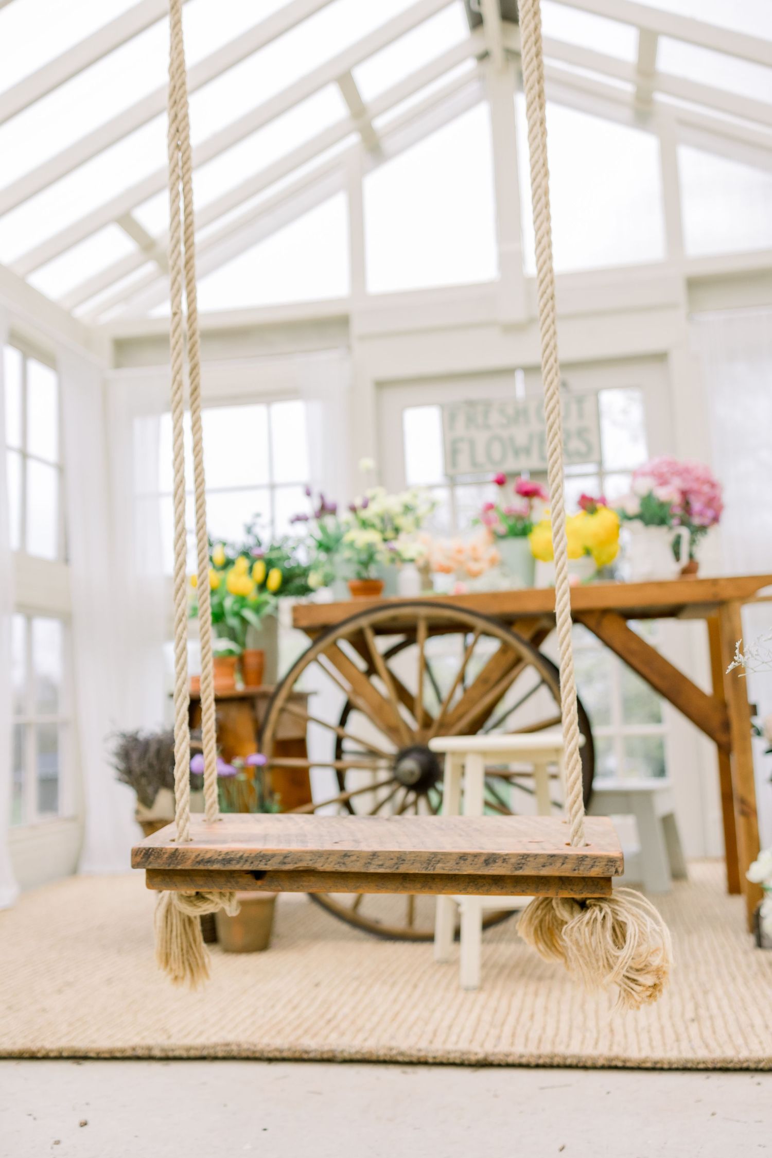 Macrame plant hangers with wooden shelves display decorative items in a bright white sunroom with natural lighting.