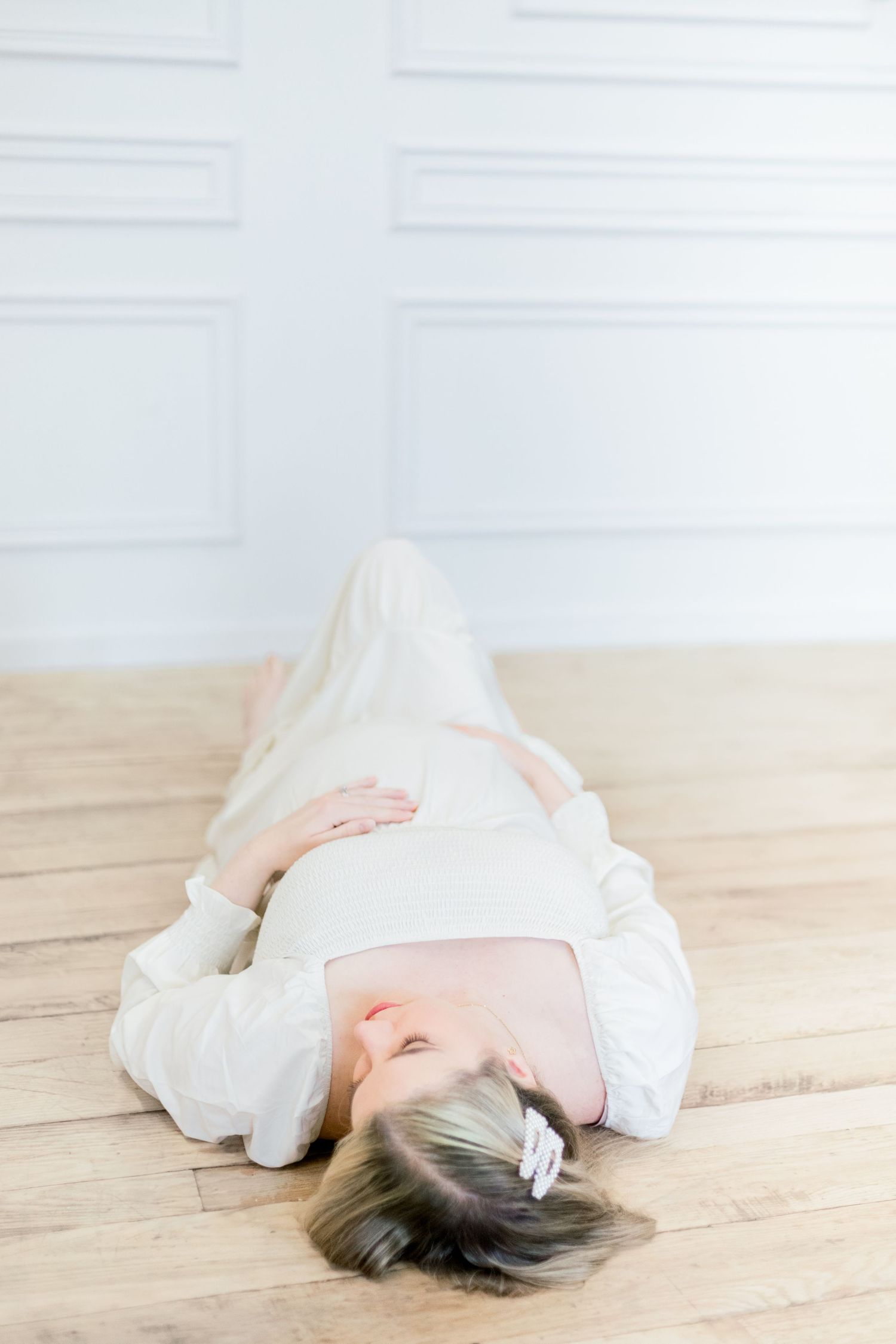 A person in a white flowing dress lies gracefully on a wooden floor in a series of artistic poses.