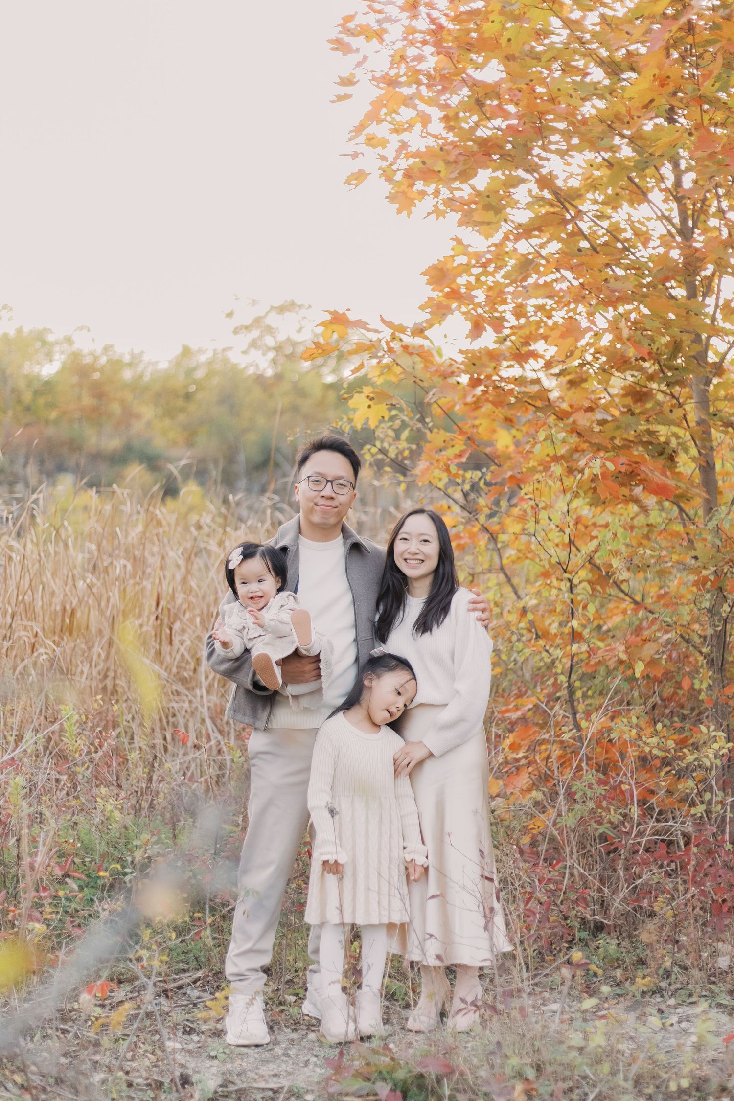 Family enjoying a tender moment together outdoors during autumn with orange foliage and tall grass in the background.