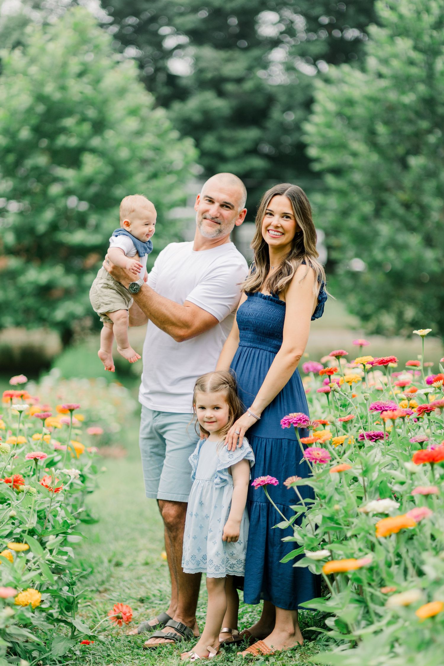 A family shares joyful moments together in a vibrant garden filled with colorful zinnias and summer flowers.