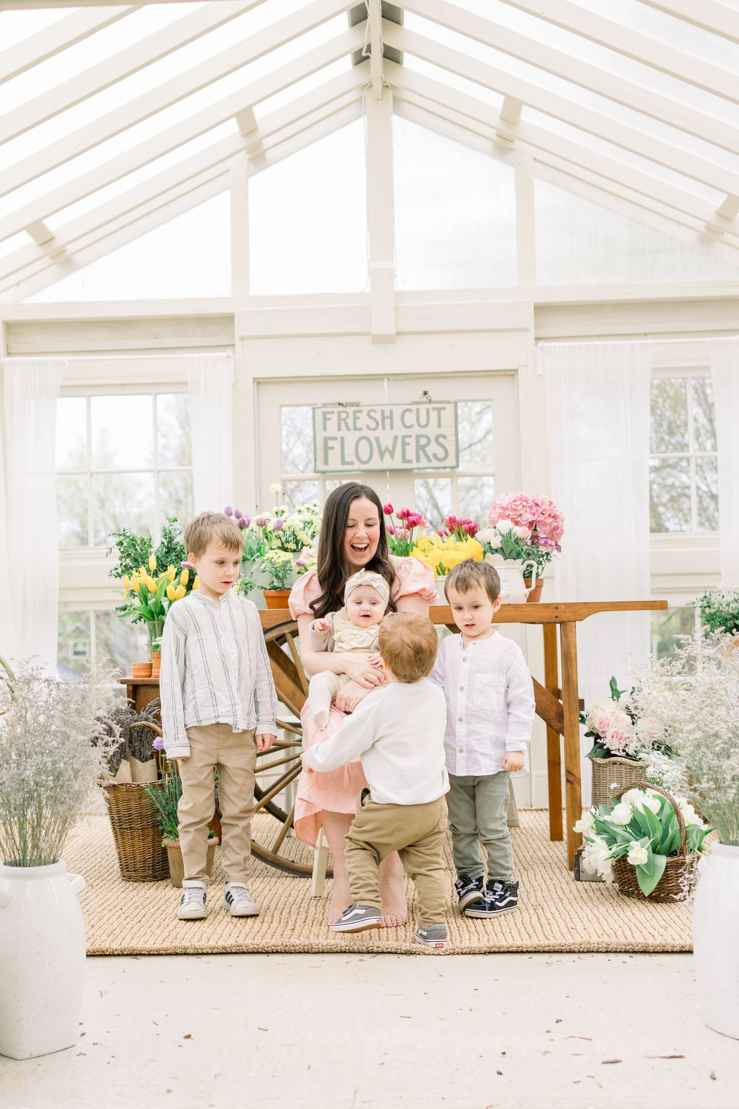 Children playing and exploring together in a bright white greenhouse with wooden floors and floral decorations.
