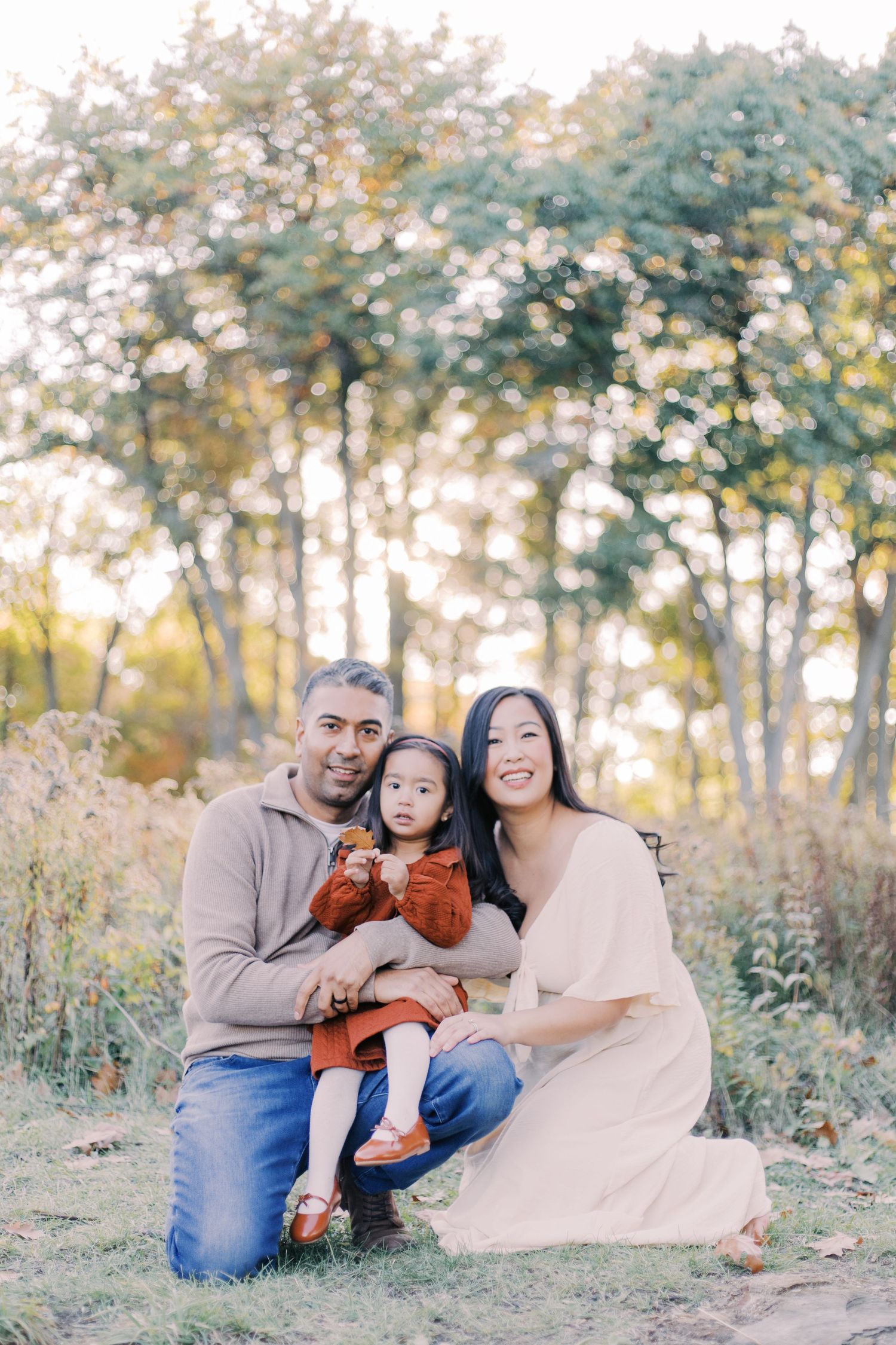A family sits together outdoors in a wooded area during golden hour, sharing joyful moments in nature.
