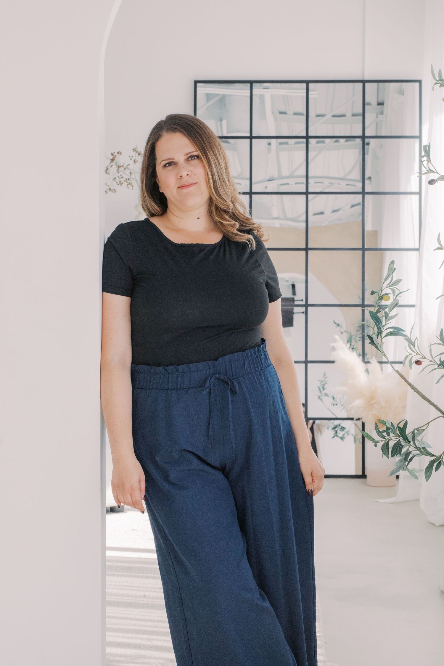 Casual outfit featuring a black t-shirt and flowy navy blue palazzo pants in a bright minimalist interior setting.