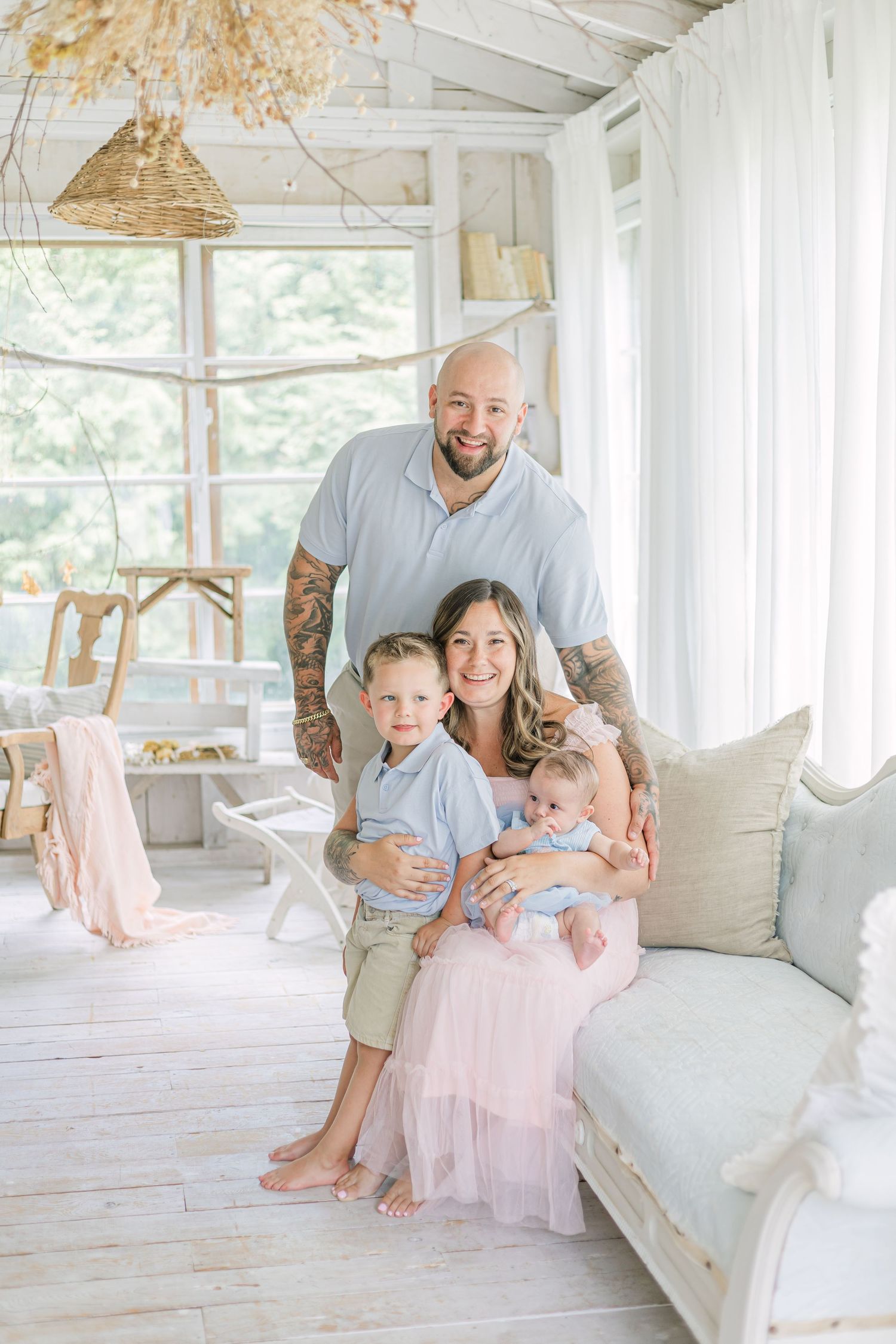 A family sits together on a white couch in a bright sunlit room with rustic decor and pendant lighting.