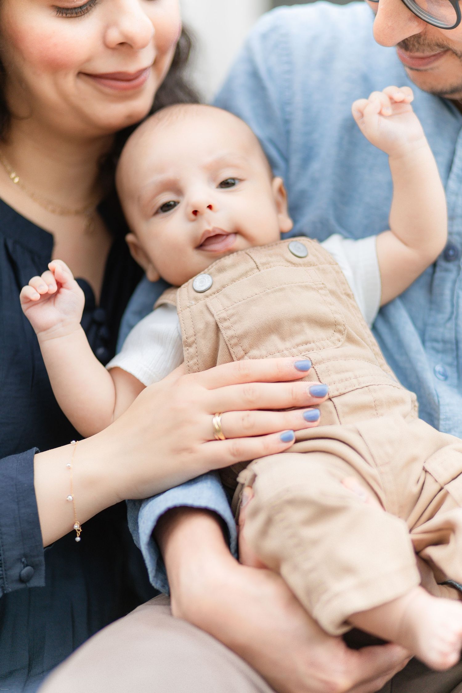 A baby in beige romper lies on parent's lap while being lovingly held and tickled in a sequence of photos.