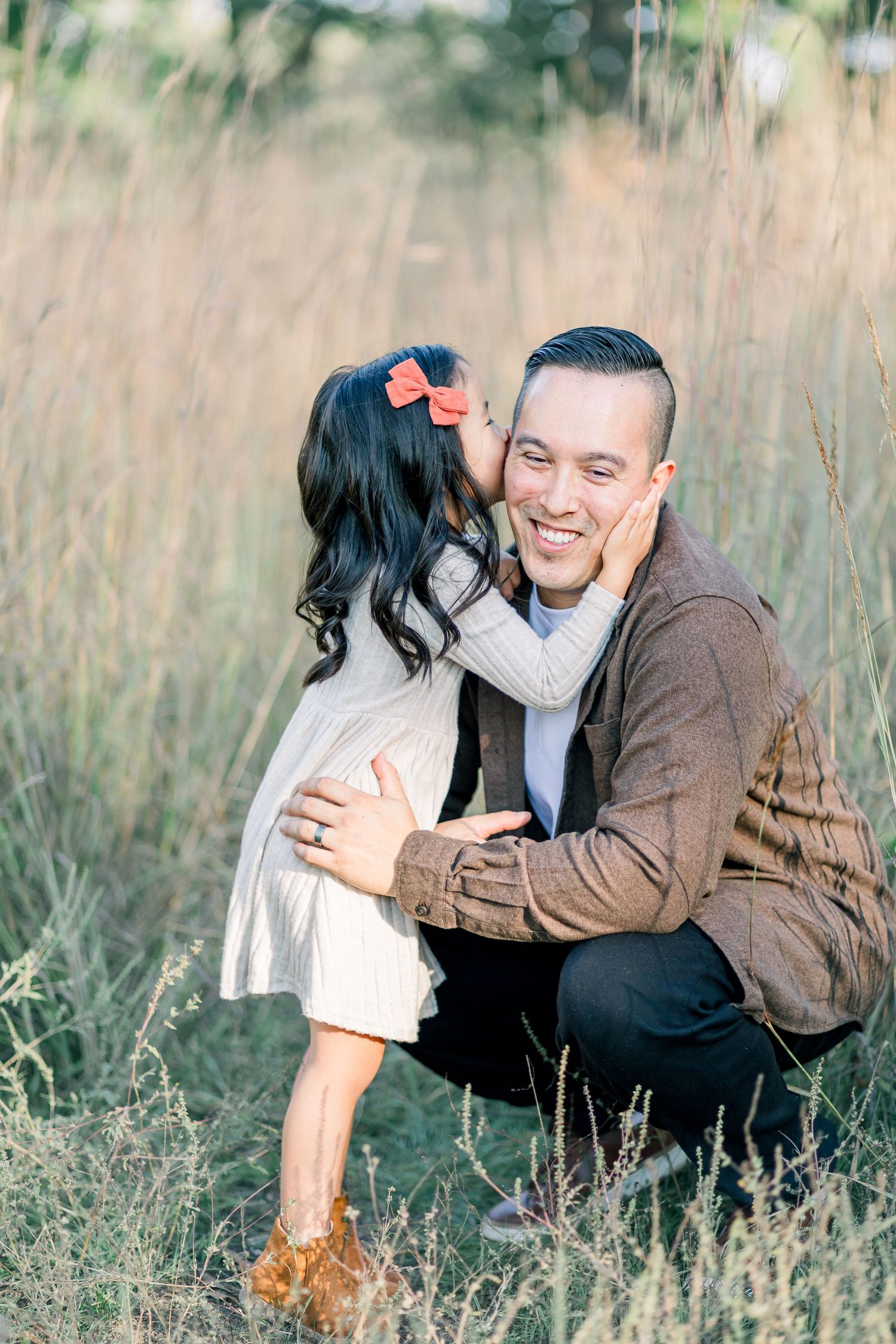 A couple embraces while sitting in tall grass during a romantic outdoor photoshoot.