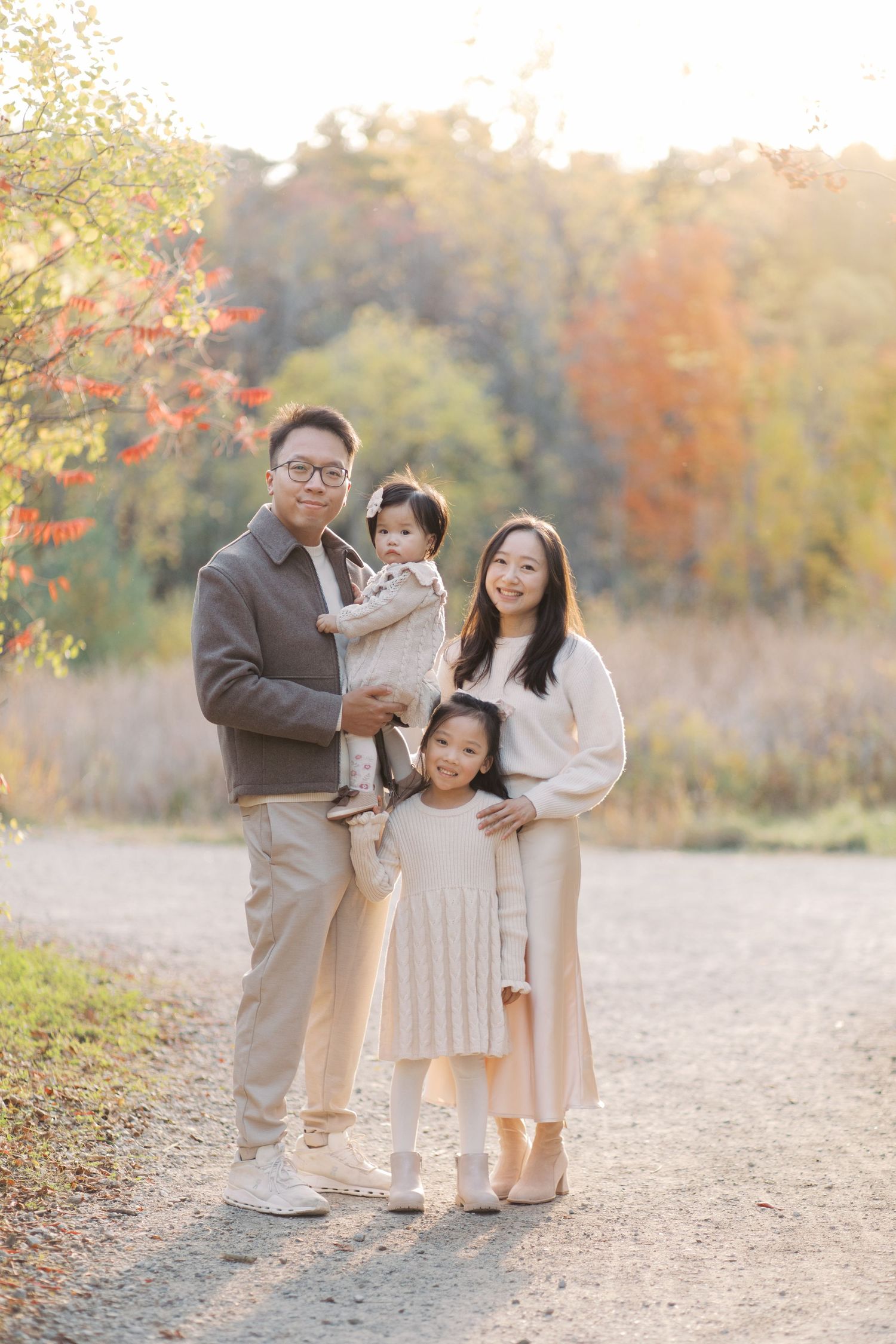 Family in coordinated beige and cream outfits poses together during autumn sunset in a natural outdoor setting.