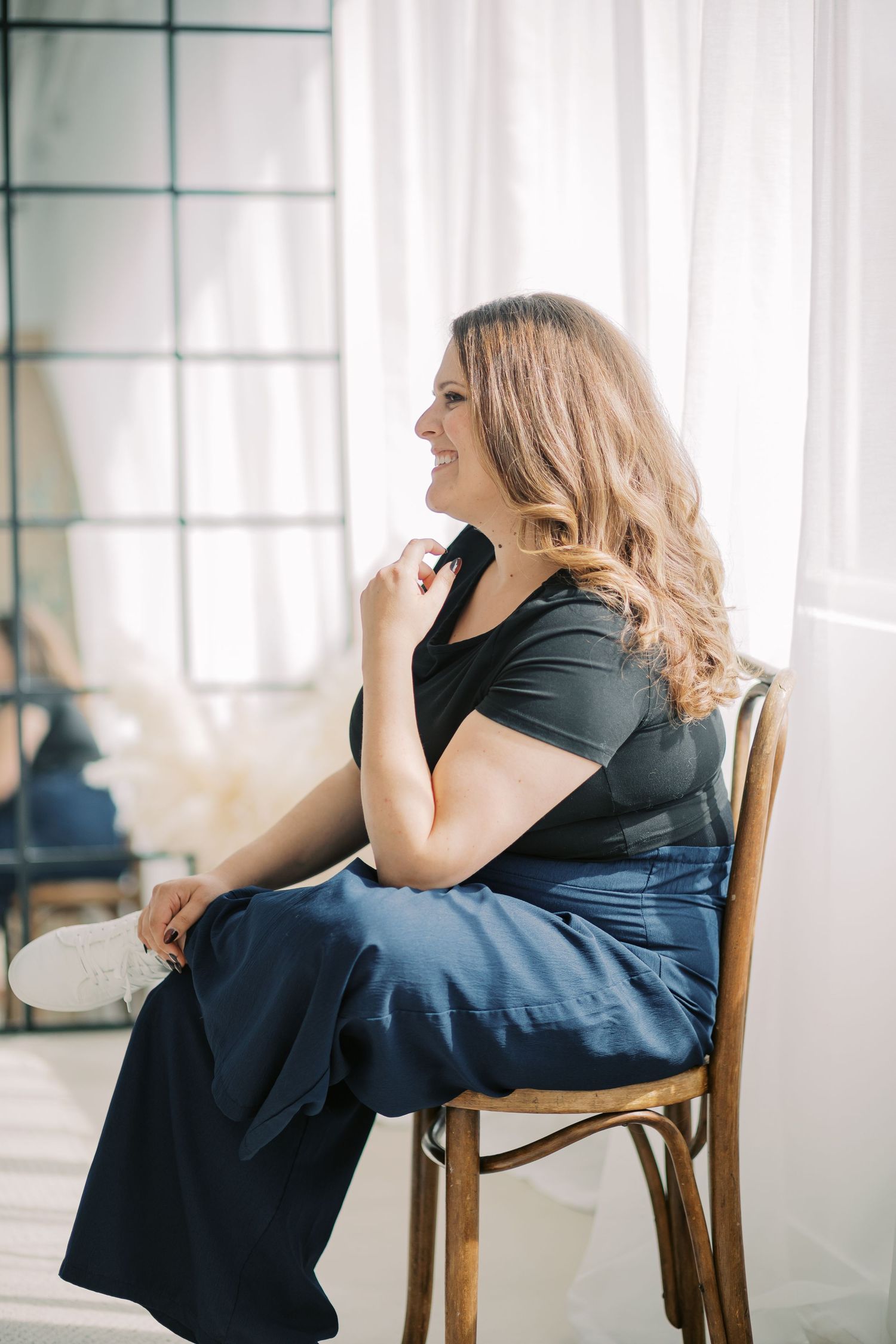 A person in a black dress sits on a wooden chair in a bright white room showing different emotional poses.